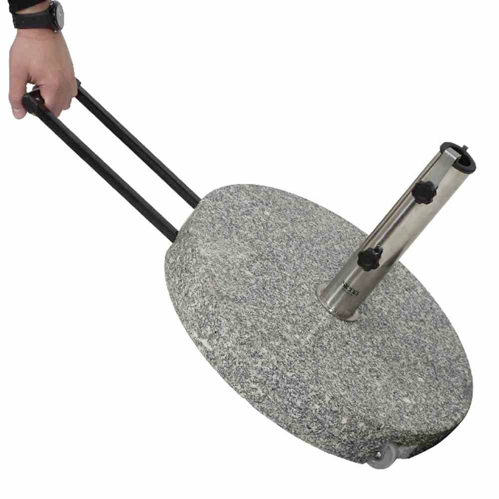 Osoba ciągnie za sobą przenośny stojak na parasole z dwoma uchwytami. Stojak posiada okrągłą, przypominającą kamień podstawę.