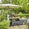 Przestrzeń na zewnątrz z miejscem do jedzenia, stacją grillową, roślinami i girlandą świetlną. Parasol przeciwsłoneczny rzuca cień na stół.