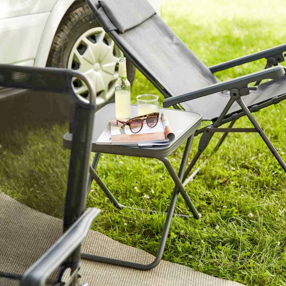 Składany krzesełko i stolik z napojem, książką i okularami przeciwsłonecznymi stoją na łące obok samochodu. Relaksujący scenariusz pikniku na świeżym powietrzu.