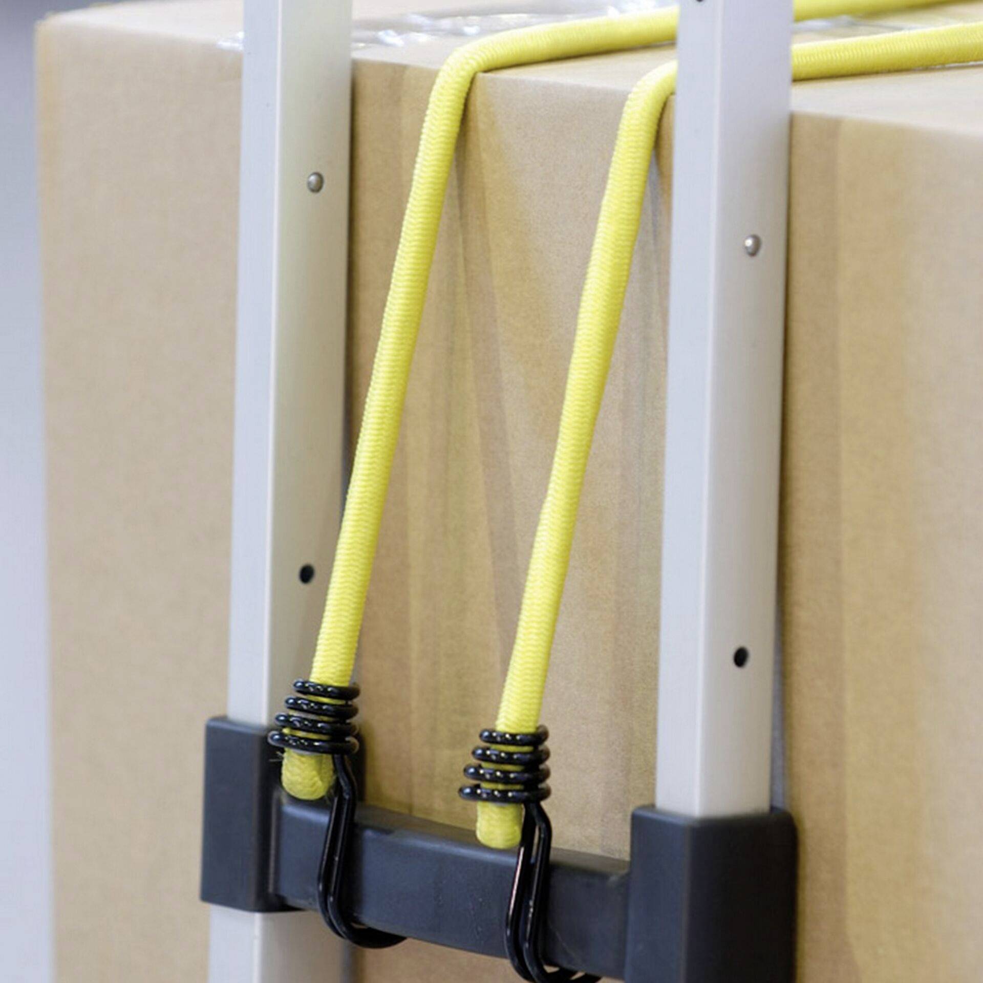 Karton przymocowany do wózka ręcznego za pomocą żółtego elastycznego pasa.