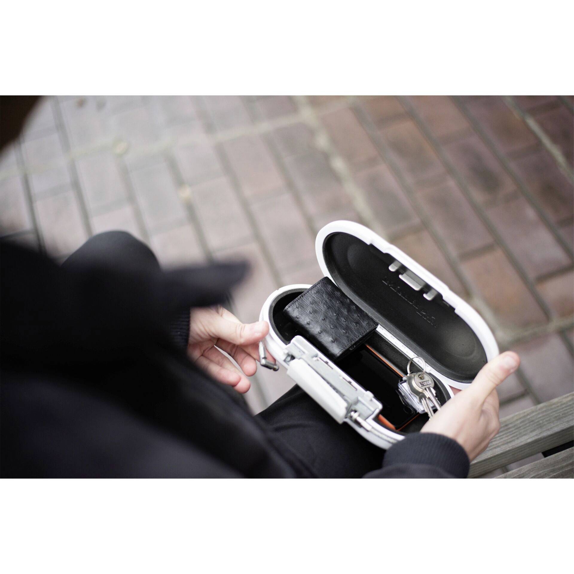 Osoba trzyma otwarte etui na okulary z okularami i małym czarnym futerałem w środku, nad podłogą we wzory.