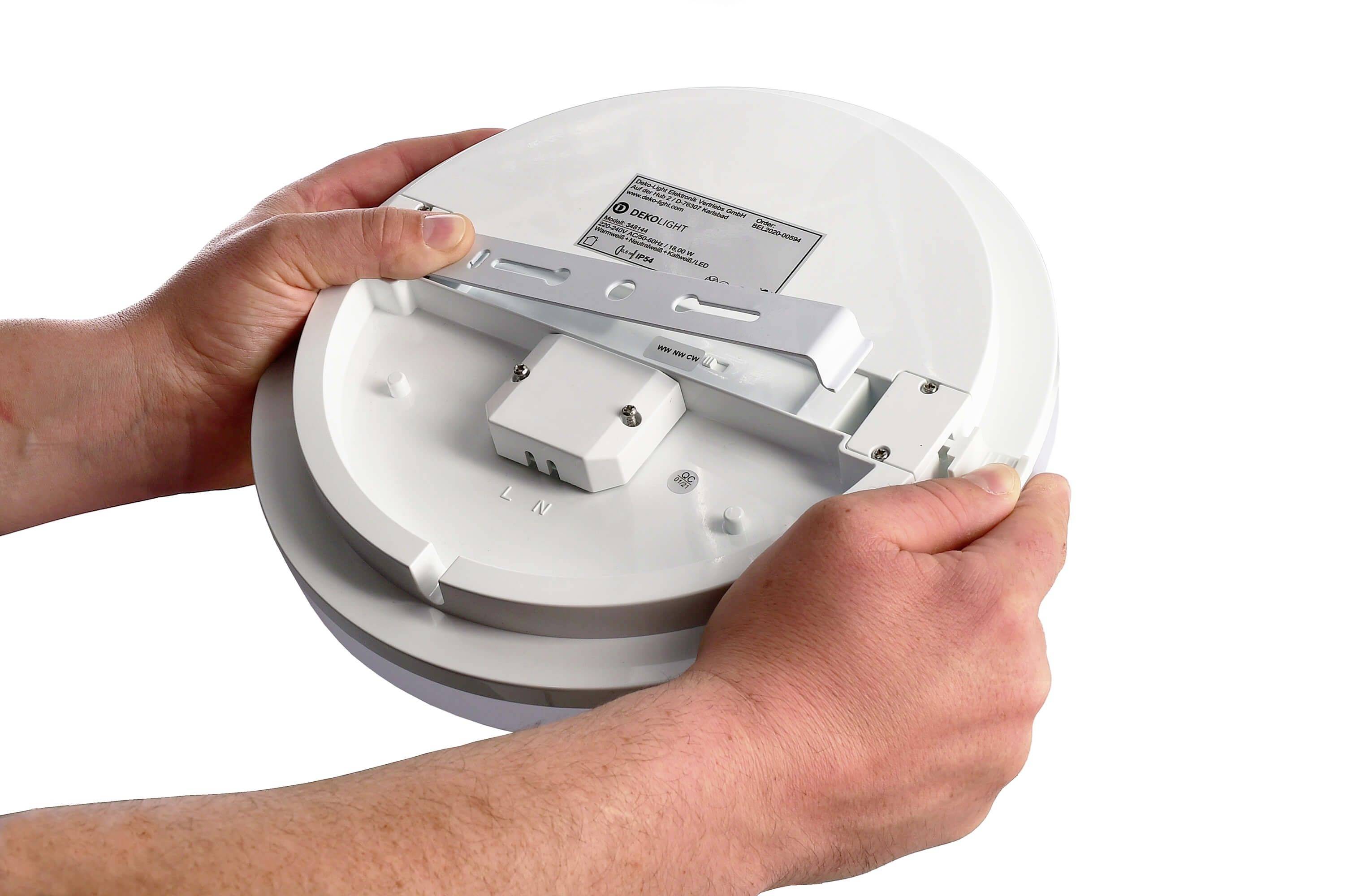 Osoba montuje okrągłą, białą lampę na uchwycie. Na tylnej stronie lampy widoczne są informacje techniczne.