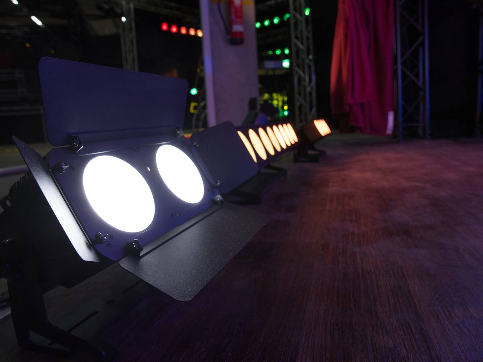Reflektory sceniczne w rzędzie na ciemnym tle, oświetlające boczne partie drewnianej powierzchni.