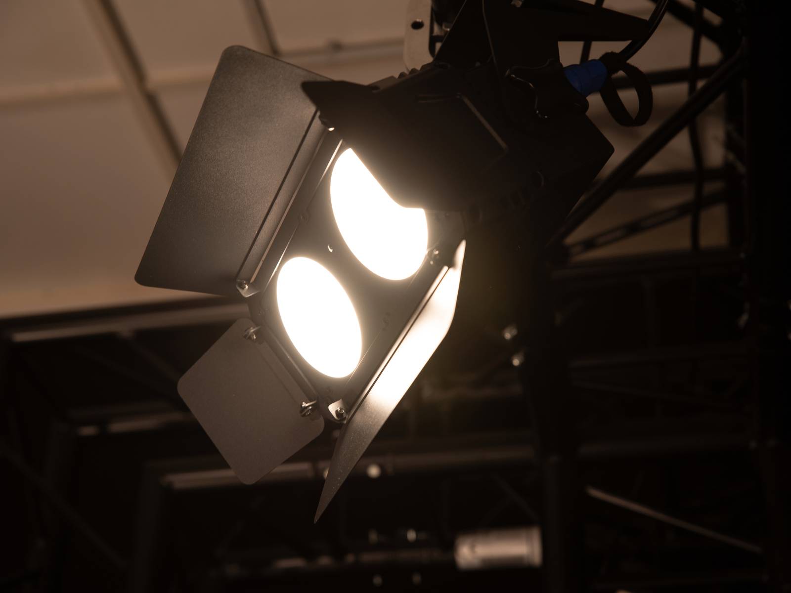 Profesjonalny reflektor z dwiema świecącymi lampami w ciemnym pomieszczeniu, gotowy do oświetlenia sceny lub przestrzeni scenicznej.