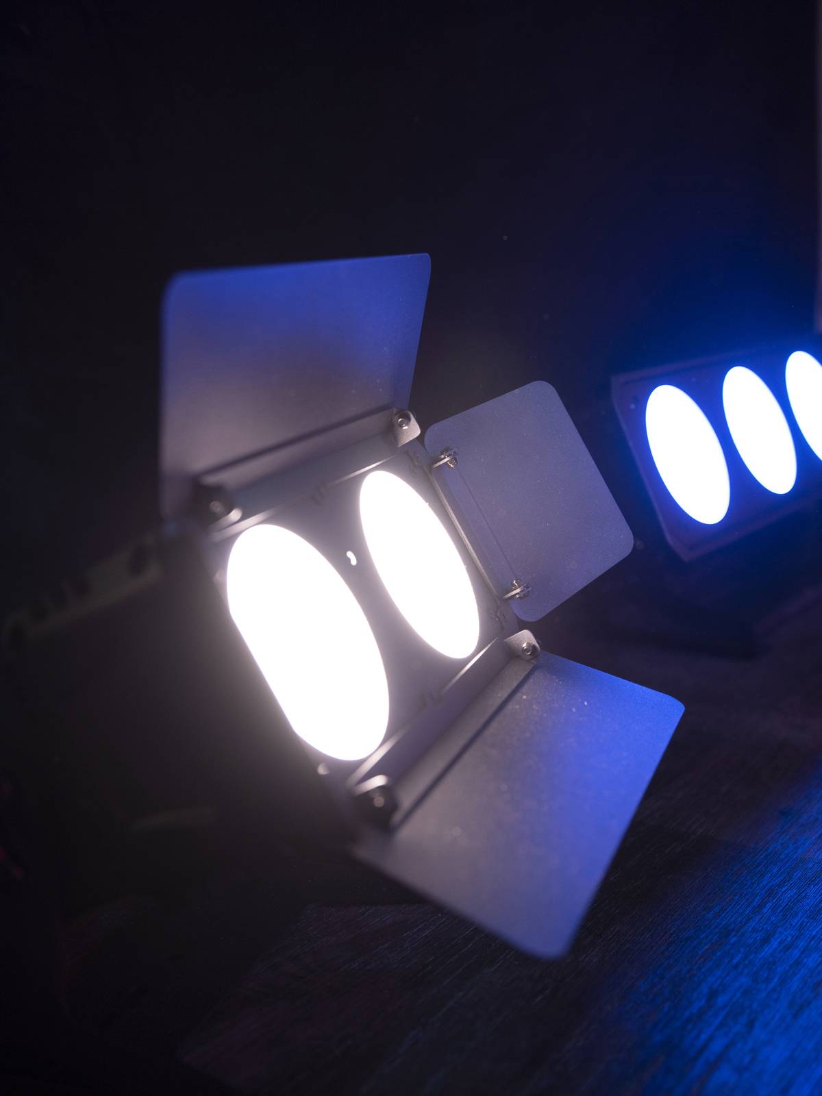 Dwa reflektory sceniczne świecą w ciemnym otoczeniu, jeden białym, a drugi niebieskim światłem.