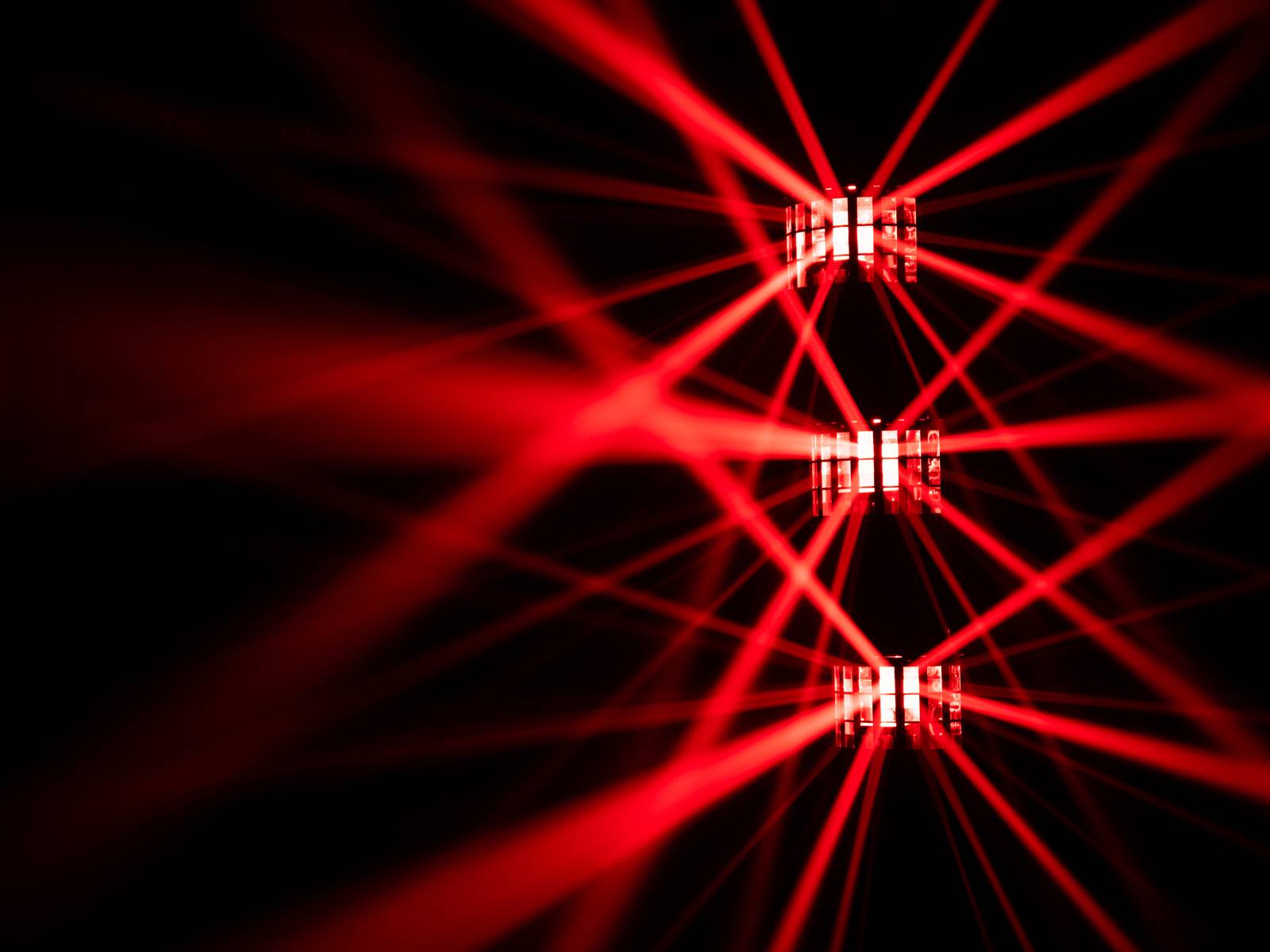 Czerwone smugi świetlne przecinają się na ciemnym tle, tworząc dynamiczny, abstrakcyjny wzór o intensywnym blasku.