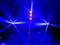 Niebieskie światło i pokaz laserowy w ciemnym pomieszczeniu, z skoncentrowanymi wiązkami światła wychodzącymi z centrum i z boku, tworzącymi dynamiczną scenografię.