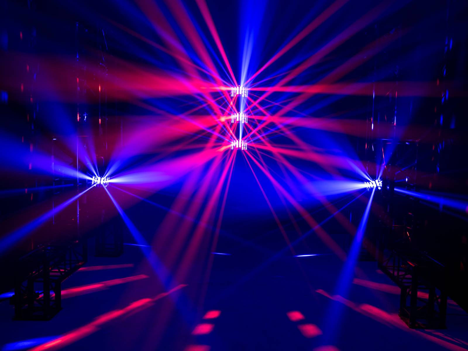 Kolorowe wiązki laserowe w kolorach niebieskim i czerwonym rozchodzą się w ciemnym pomieszczeniu różnymi kierunkami, tworząc imponujący spektakl świetlny.