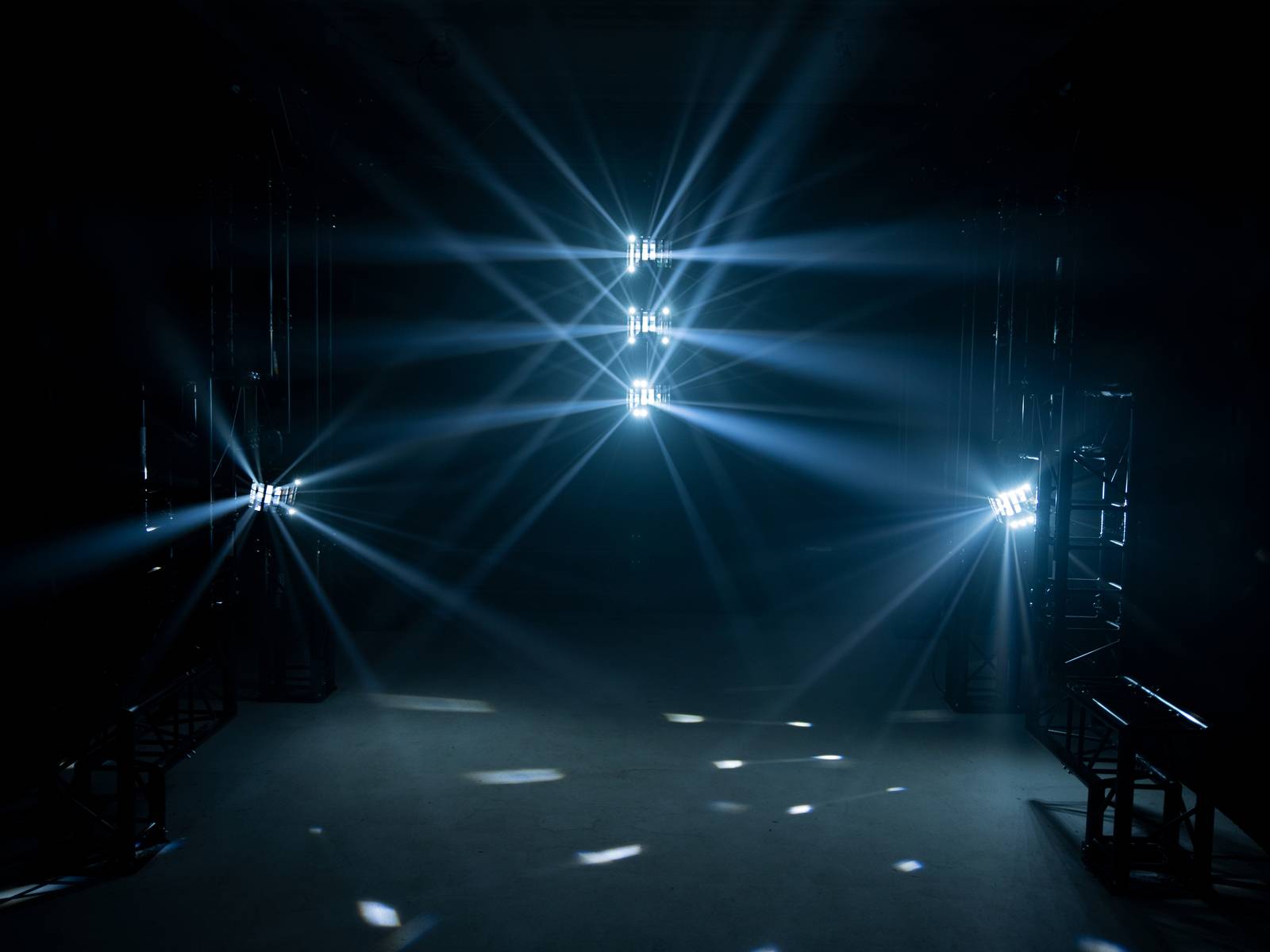 Ciemne pomieszczenie z jasnymi reflektorami, które rzucają na podłogę i ściany promieniste wzory świetlne.