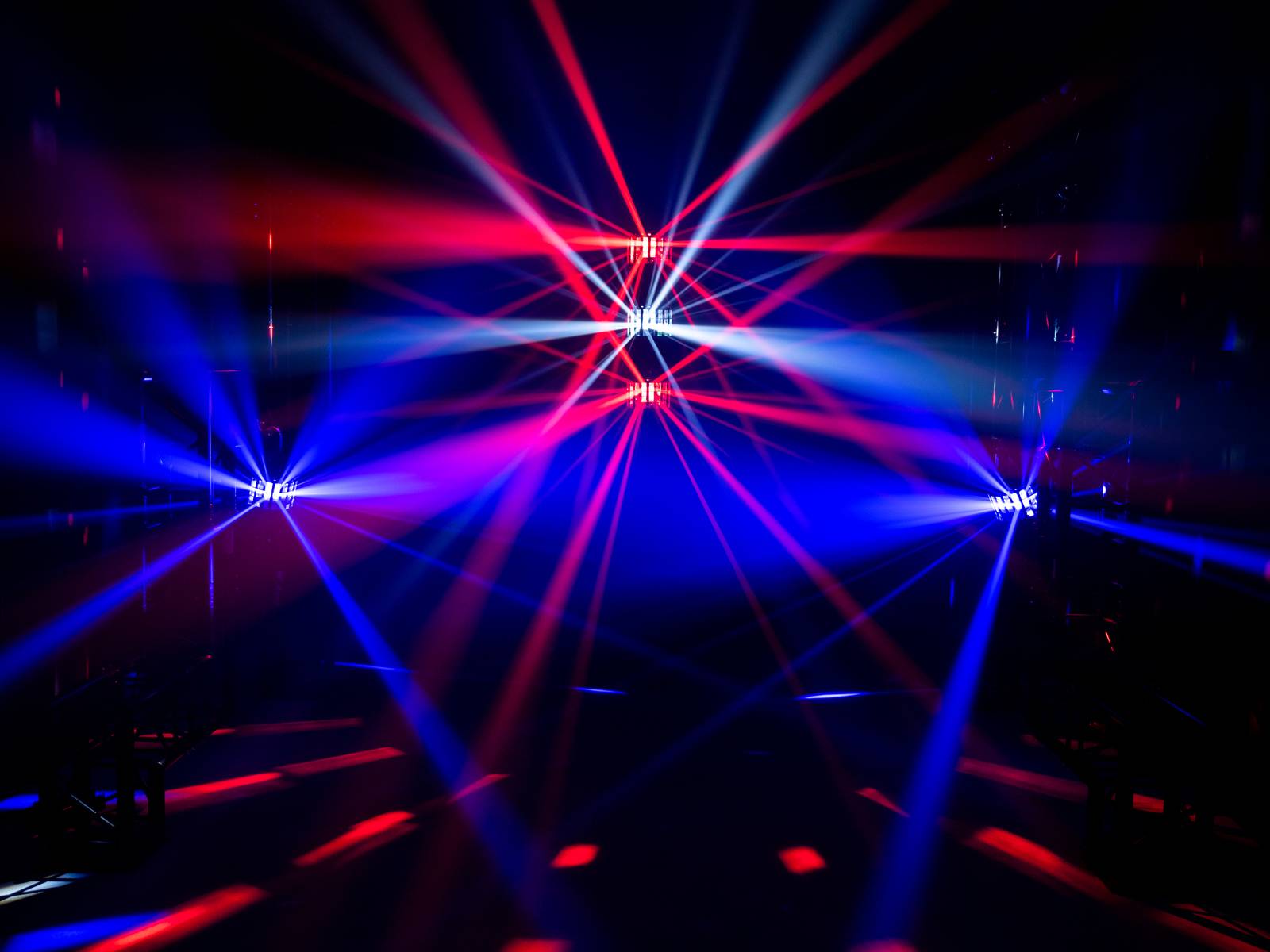 Pokaz świateł z czerwono-niebieskimi promieniami w ciemnej przestrzeni, rozchodzącymi się w różnych kierunkach; tworzy dynamiczną, futurystyczną atmosferę.