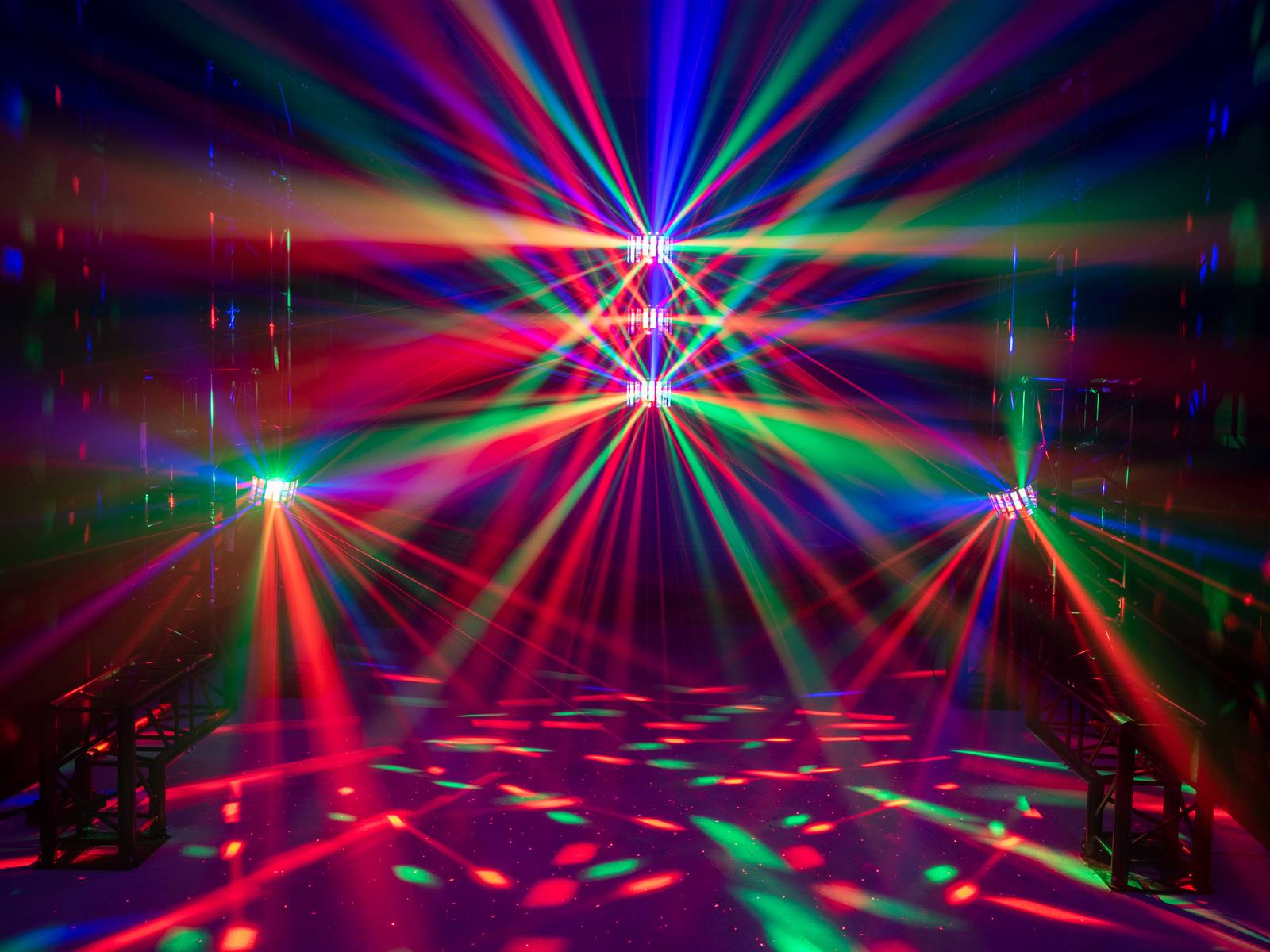 Kolorowa gra świateł z czerwonymi, zielonymi i niebieskimi promieniami, które rozchodzą się z różnych punktów w ciemnym pomieszczeniu.