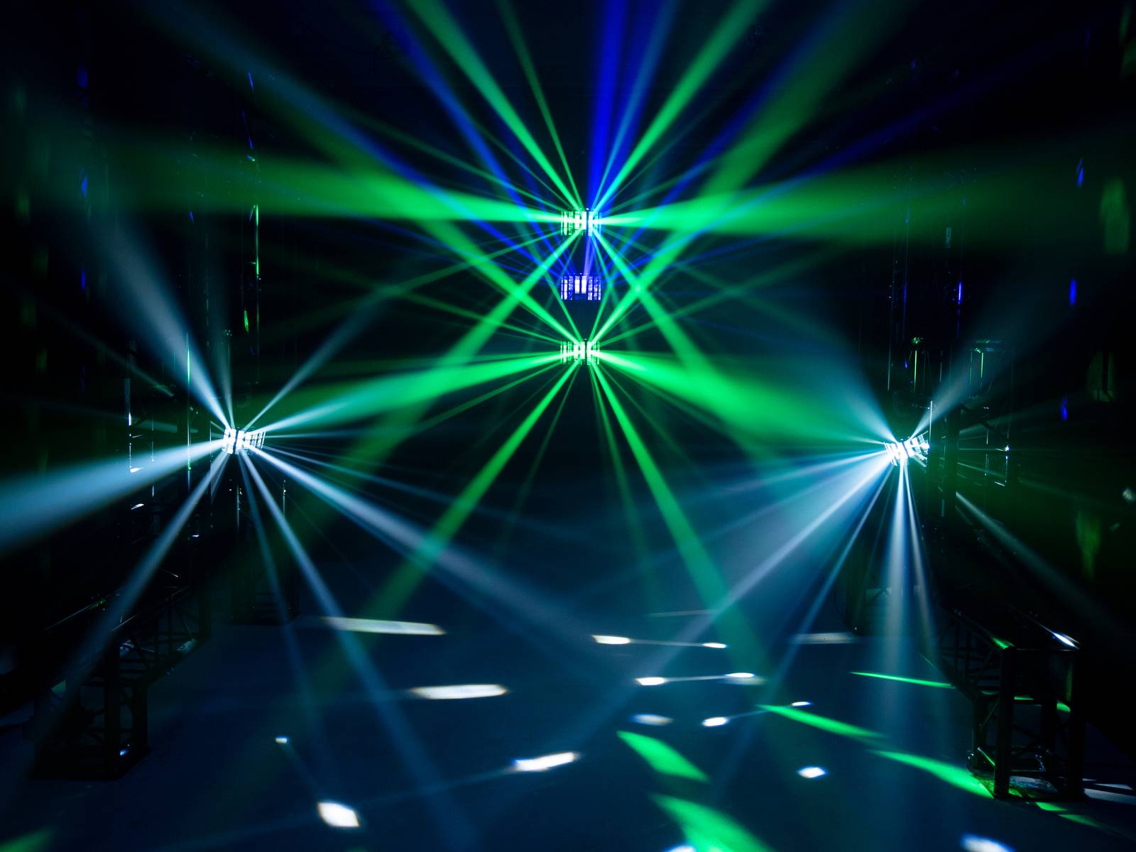 Kolorowe smugi świetlne w odcieniach niebieskiego i zielonego przecinają się w ciemnym pomieszczeniu, tworząc żywy, futurystyczny wzór.