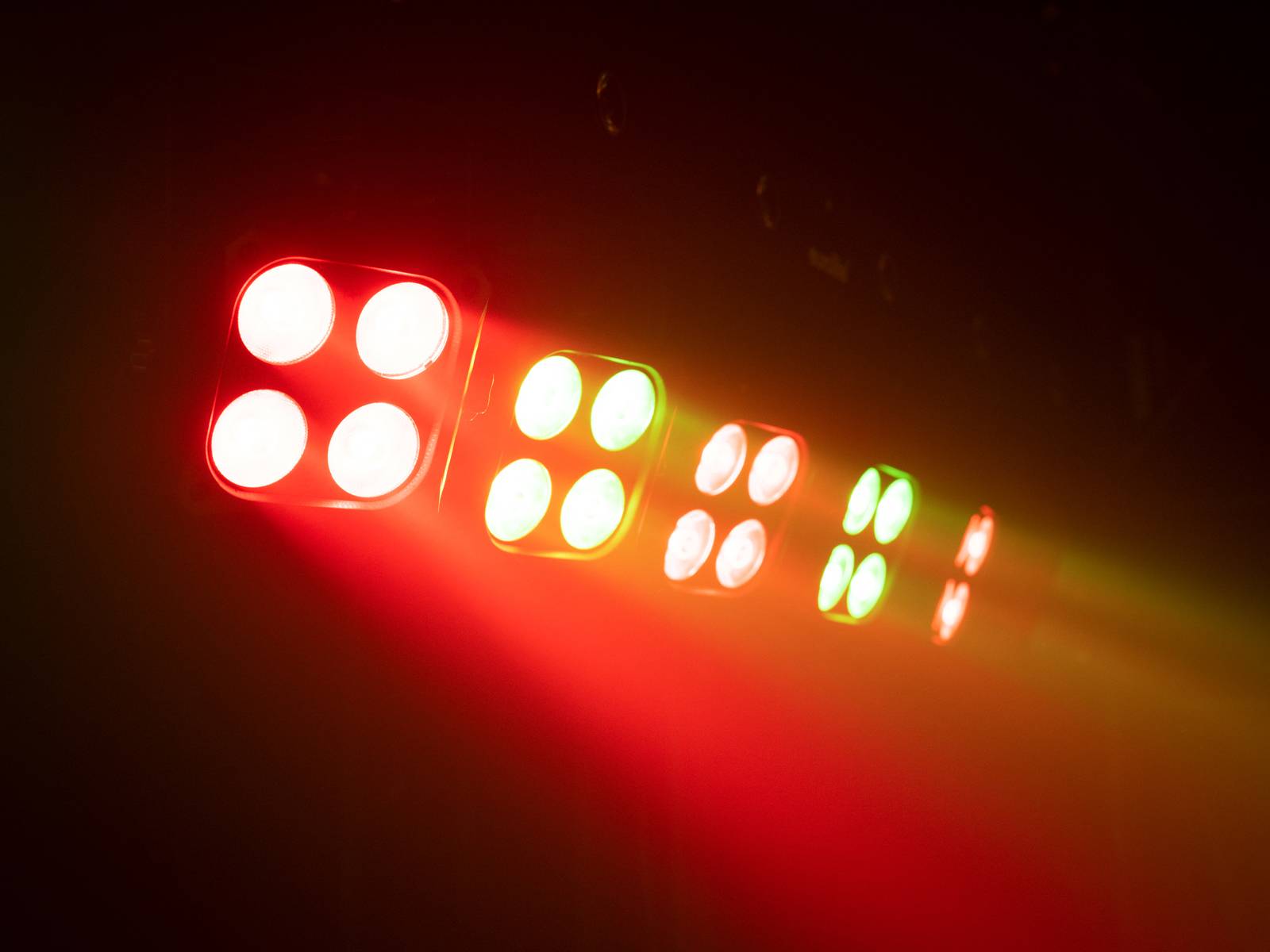 Żywy wzór świetlny z naprzemiennie ustawionymi czerwonymi, zielonymi i białymi reflektorami, ułożonymi w rzędach i emitującymi światło w przestrzeń.