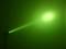 Zielony promień laserowy świeci od lewej do prawej przez ciemne pomieszczenie, tworząc świecący punkt na ścienie.