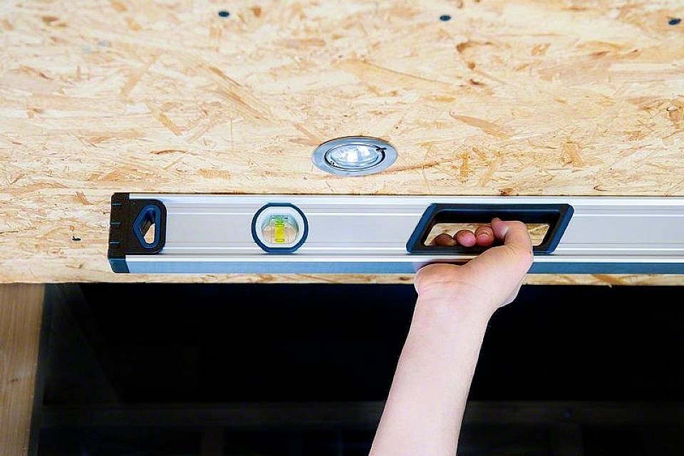 Ręka trzyma poziomicę przy desce drewnianej, sprawdzając jej wyrównanie.