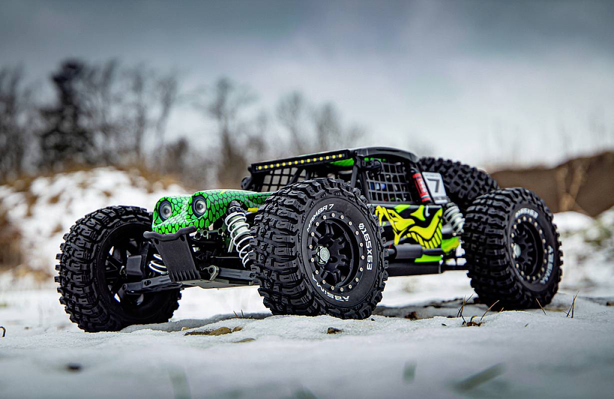 Zdalnie sterowane auto z dużymi, solidnymi oponami i rzucającą się w oczy zieloną i czarną farbą stoi ukośnie na śniegu.