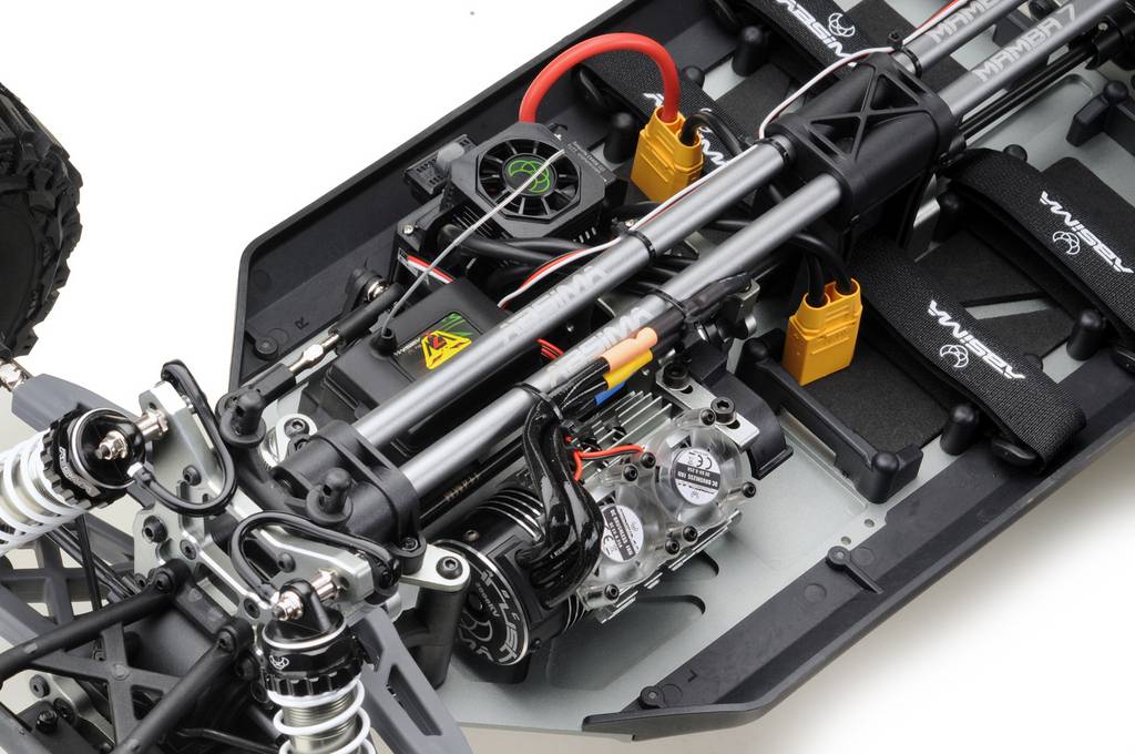 Obraz przedstawia wnętrze samochodu zdalnie sterowanego, wyraźnie ukazujący silnik, przewody oraz zawieszenie z amortyzatorami.