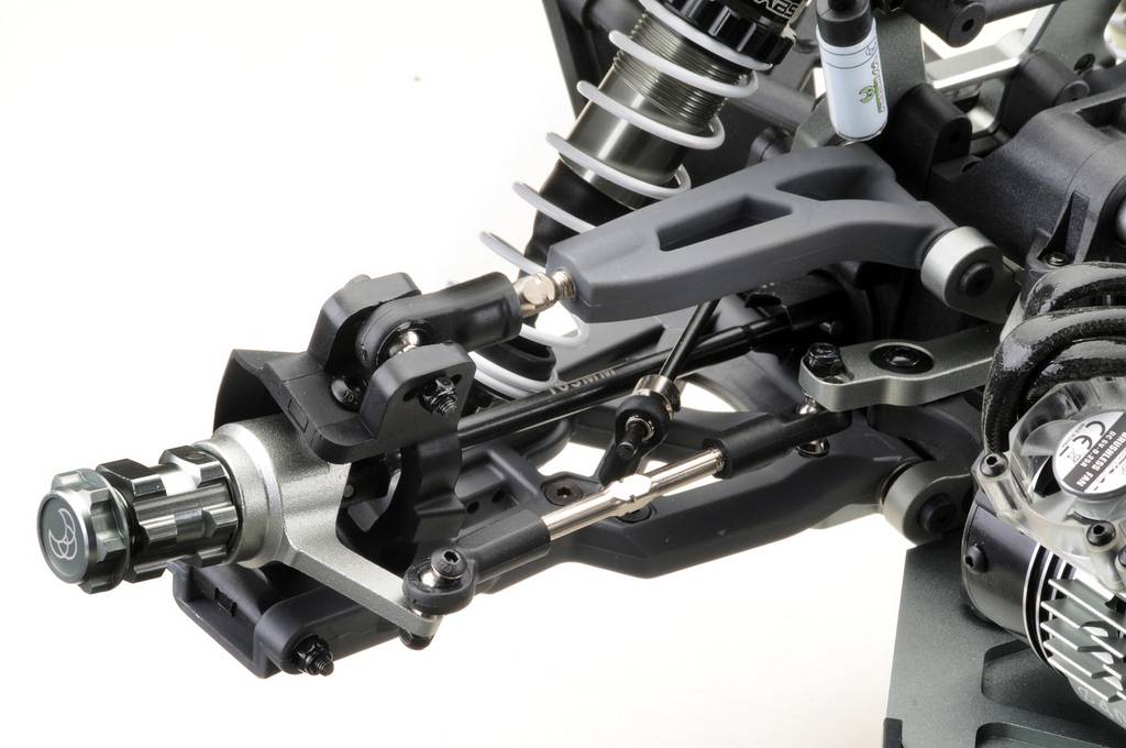 Zbliżenie podwozia modelu samochodu z widocznym zawieszeniem i zwrotnicą. Szczegółowe przedstawienie komponentów i materiałów.