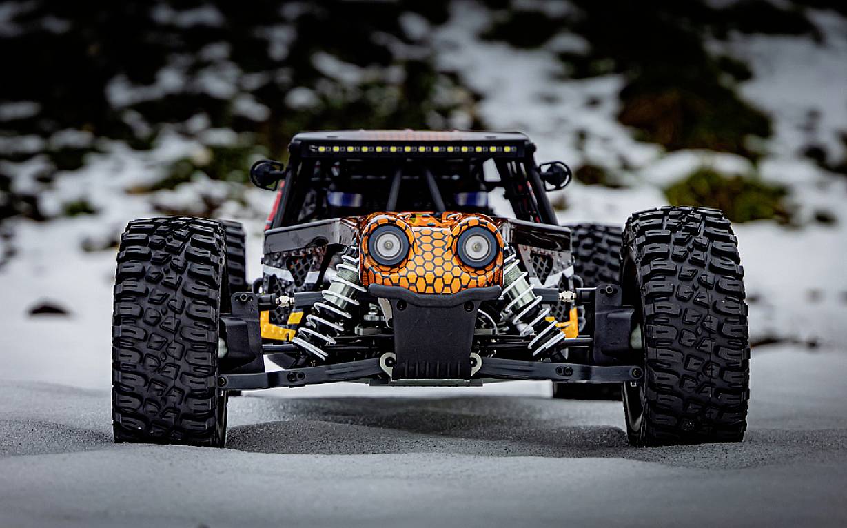 Zdalnie sterowany samochód z dużymi terenowymi oponami, stojący przodem na śniegu. Projekt nadwozia przypomina twarz.