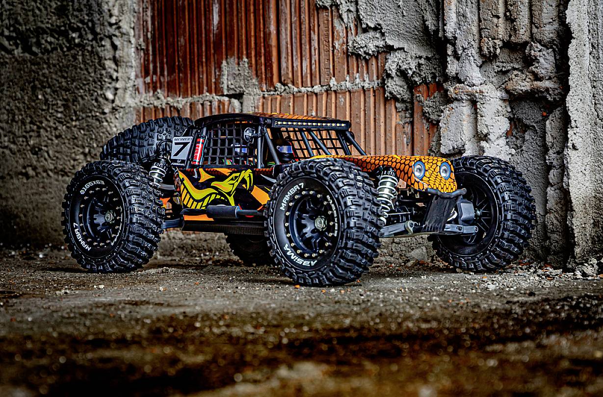 Zdalnie sterowany samochód z dużymi kołami i kolorowym wzornictwem stoi przed ścianą z surowego betonu i cegieł.