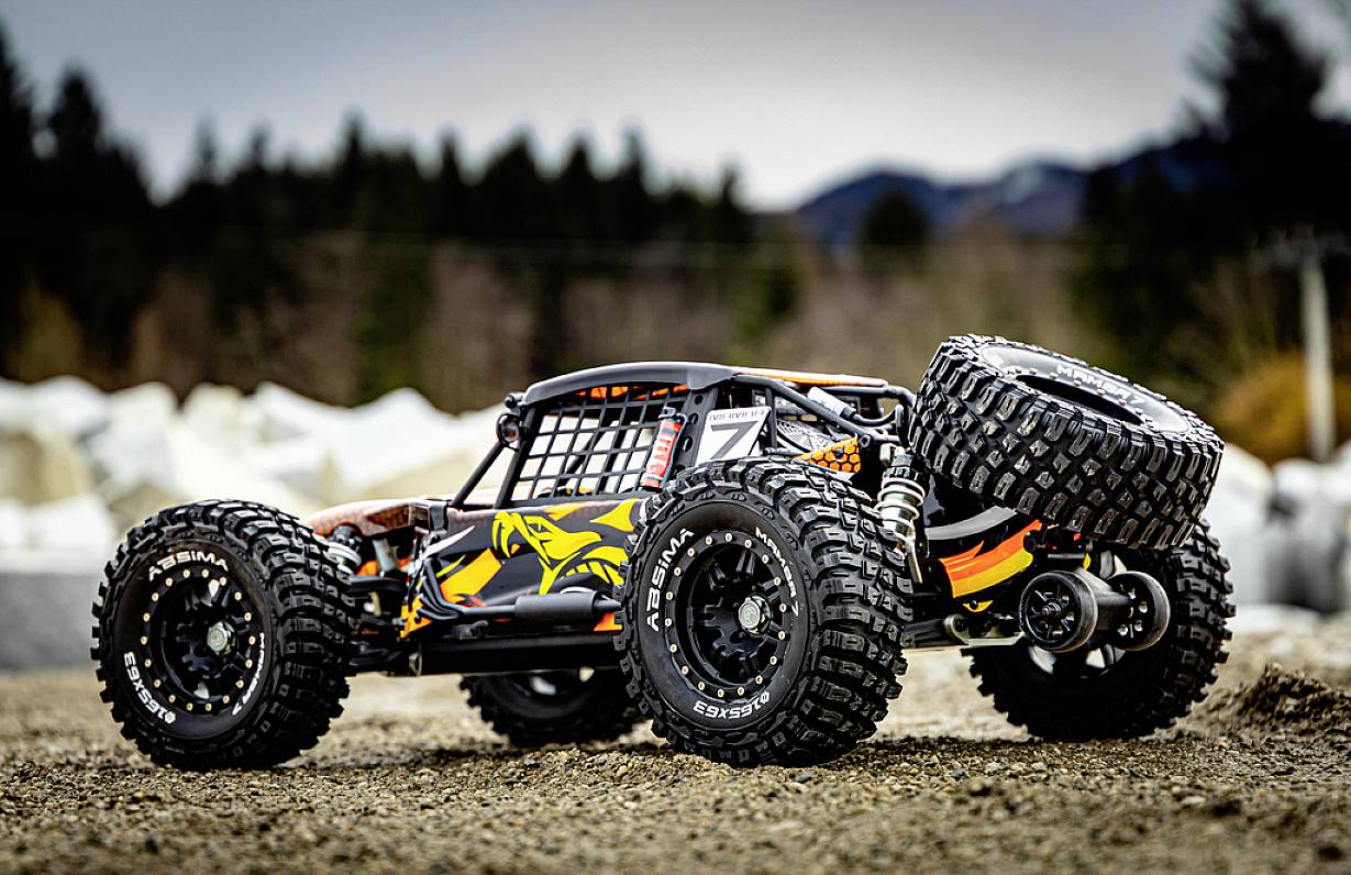 Zdalnie sterowany, terenowy model samochodu z solidnymi oponami stoi na nieutwardzonej drodze, otoczony rozmytym tłem lasu.