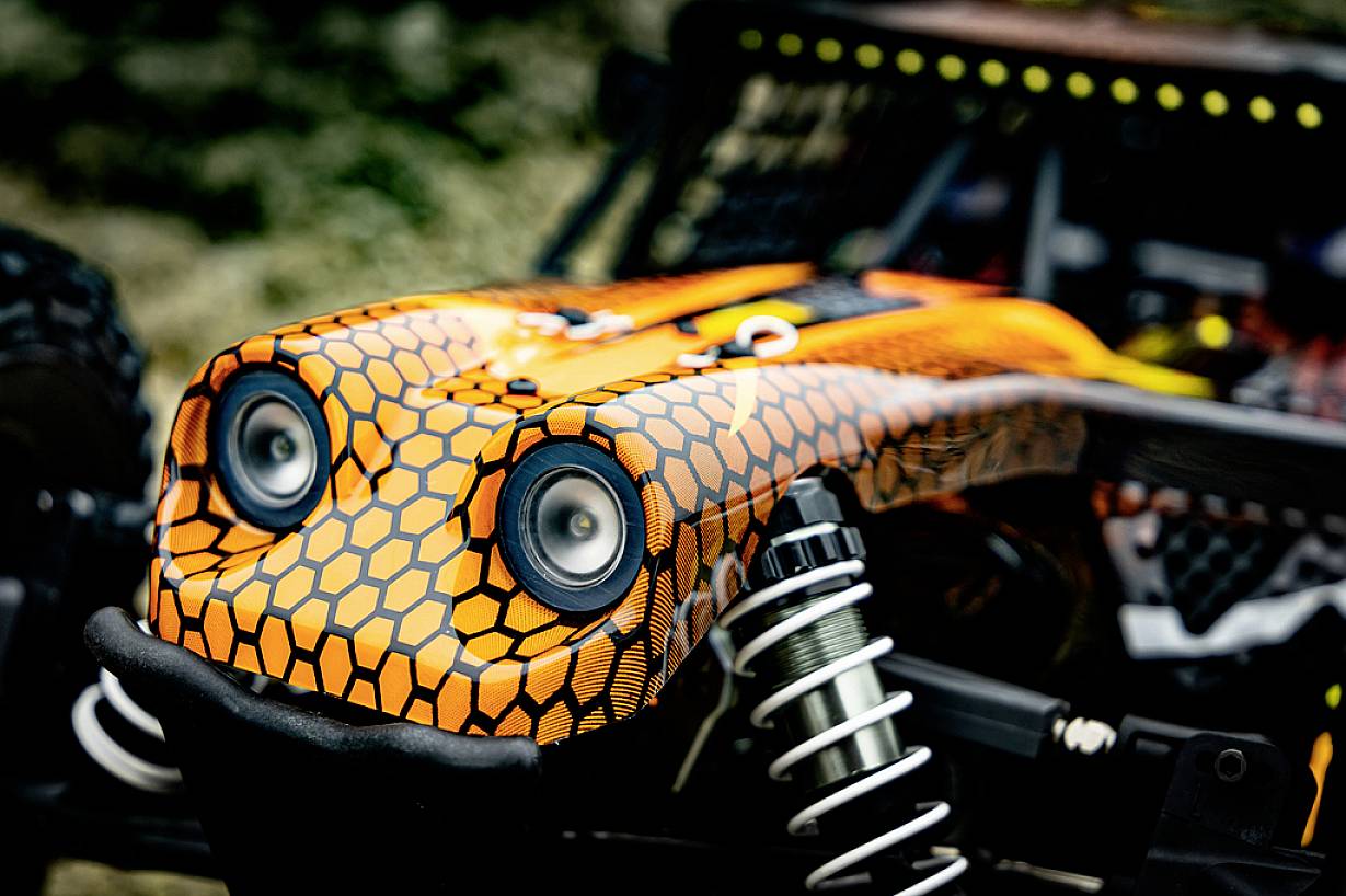 Zbliżenie zdalnie sterowanego samochodu terenowego w pomarańczowo-czarnym wzorze plastra miodu, z widocznymi amortyzatorami.