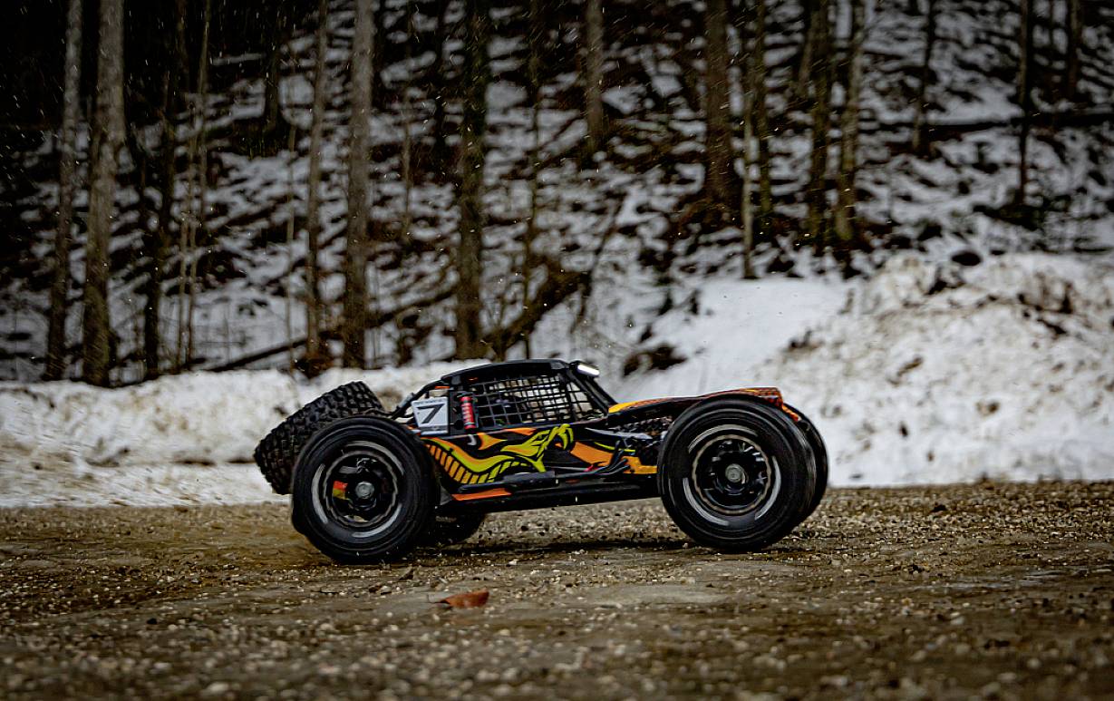 Zdalnie sterowany samochód poruszający się po zaśnieżonej leśnej drodze. Pojazd posiada rzucający się w oczy, kolorowy design.