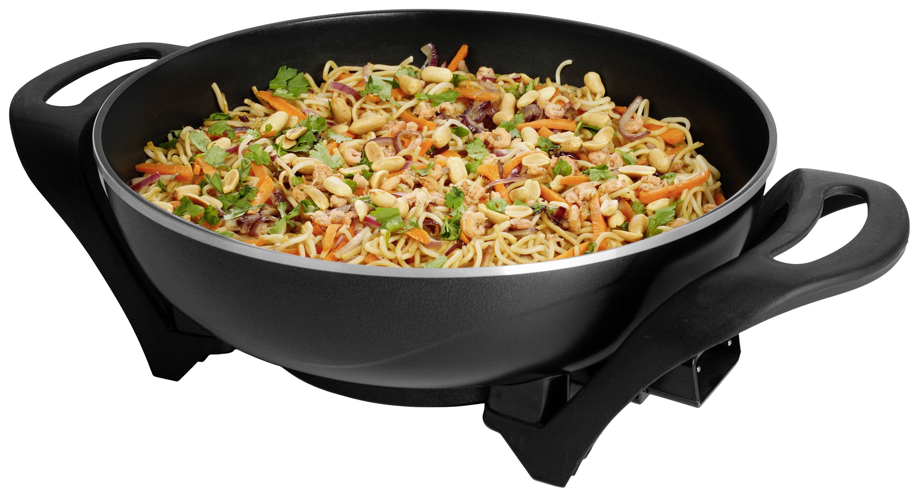 Duża, czarna patelnia wypełniona smażonym makaronem, kolorowanymi warzywami i ziołami. Patelnia posiada dwa uchwyty.