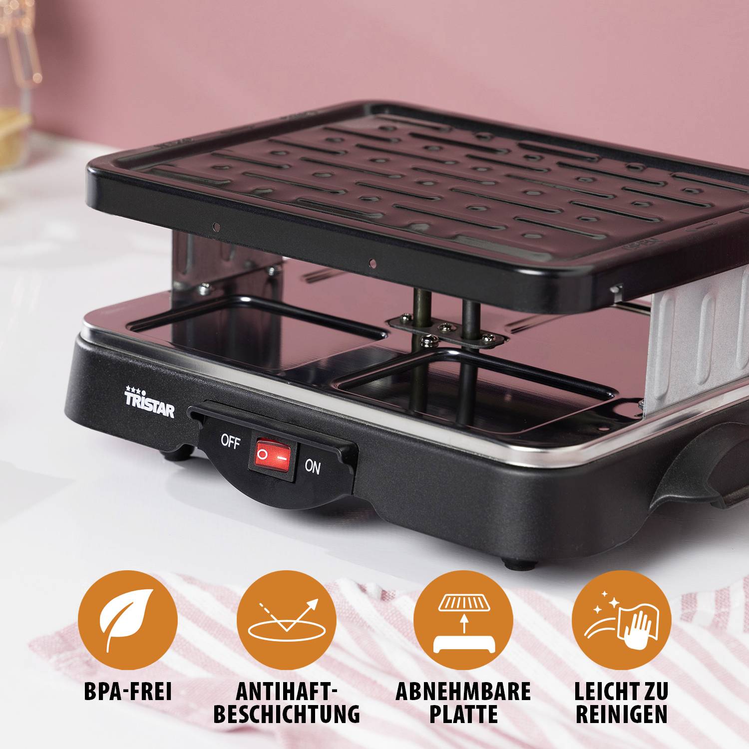 Elektryczny grill na stole. Symbole poniżej wskazują: bez BPA, powłoka nieprzywierająca, zdejmowana płyta, łatwy w czyszczeniu.