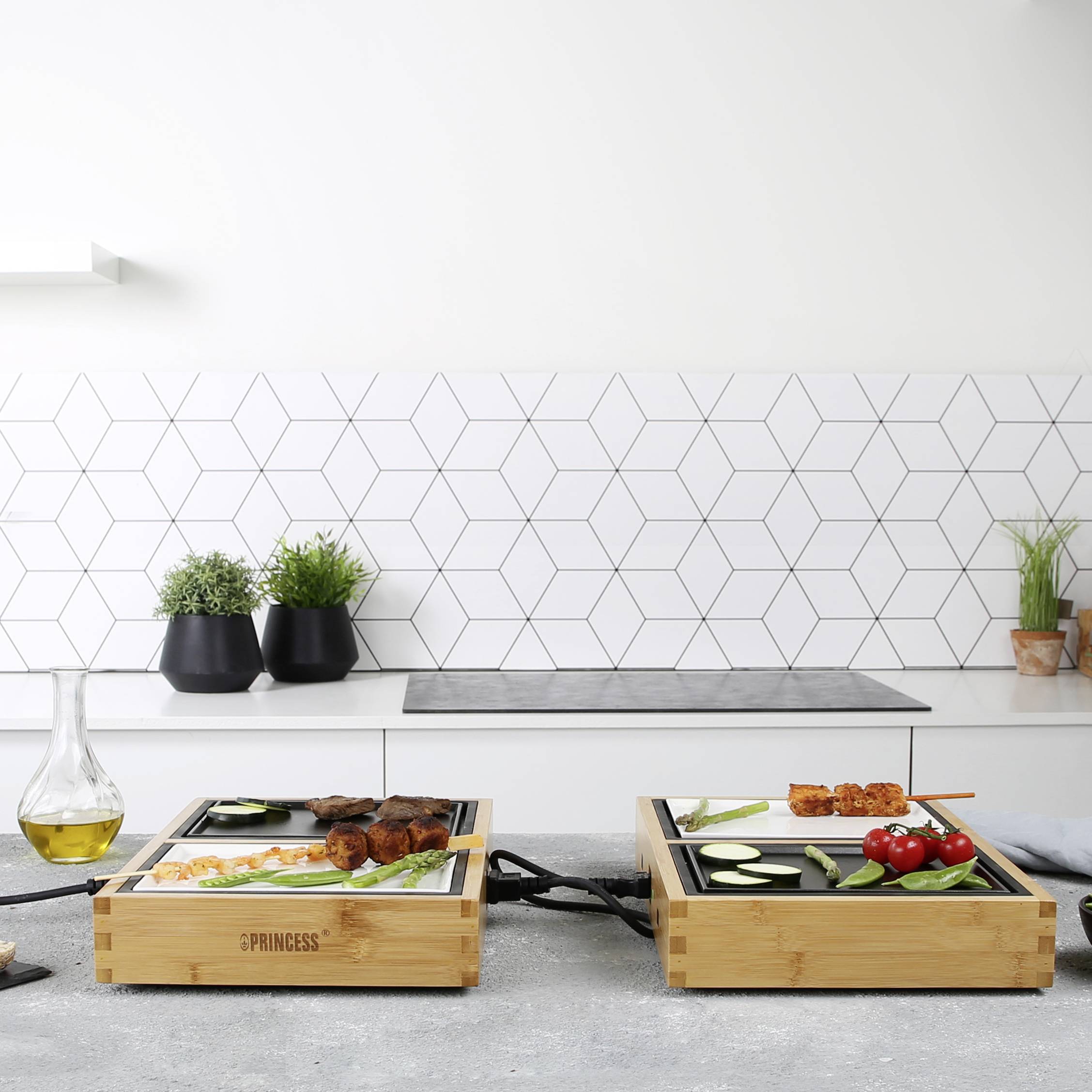 Nowoczesna przestrzeń kuchenna z elektrycznym grillem, warzywami i mięsem ułożonymi na deskach do krojenia, otoczona minimalistycznym designem.