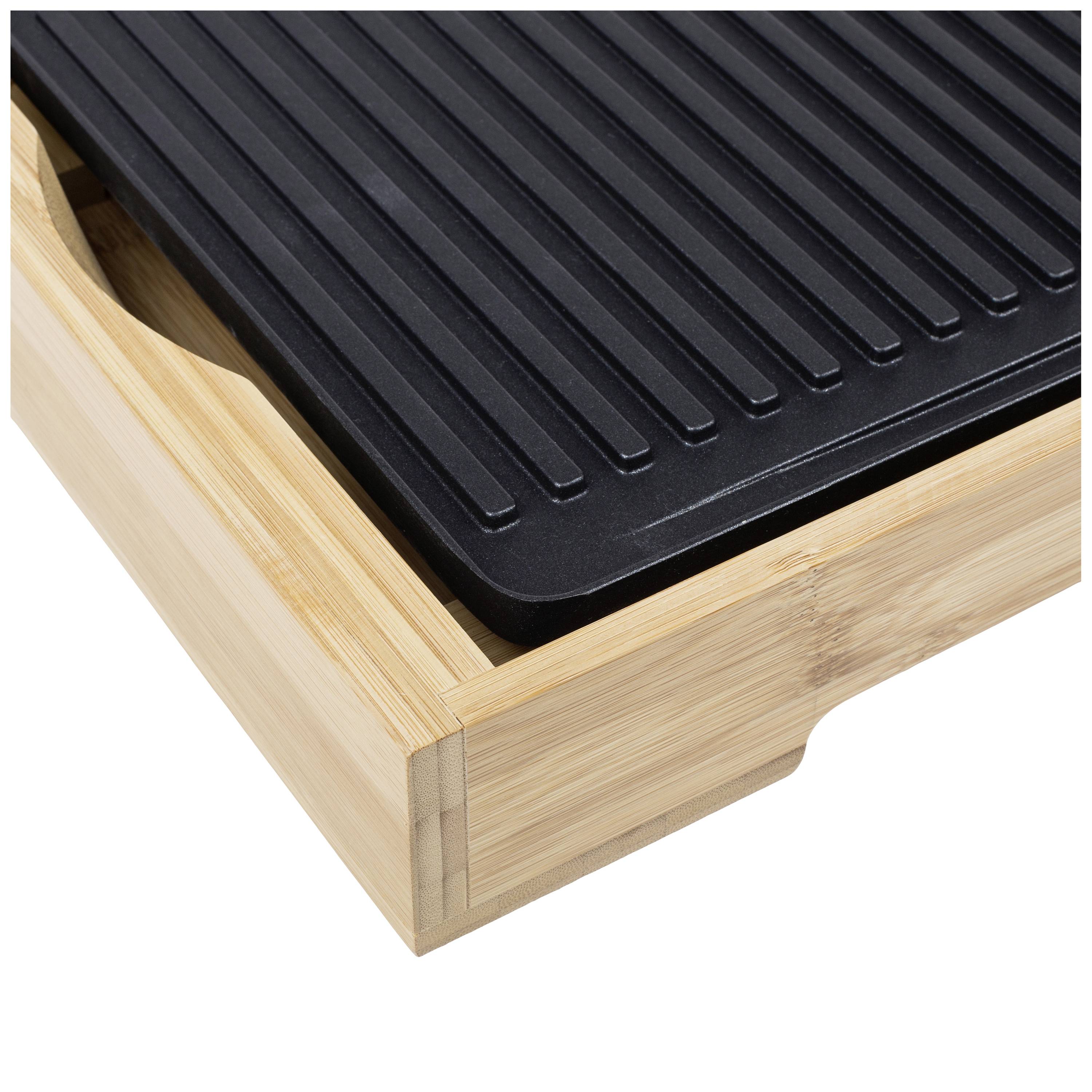 Czarna płyta grillowa na drewnianej tacy. Płyta posiada rowki i leży po prawej stronie prostokątnej drewnianej tacy.