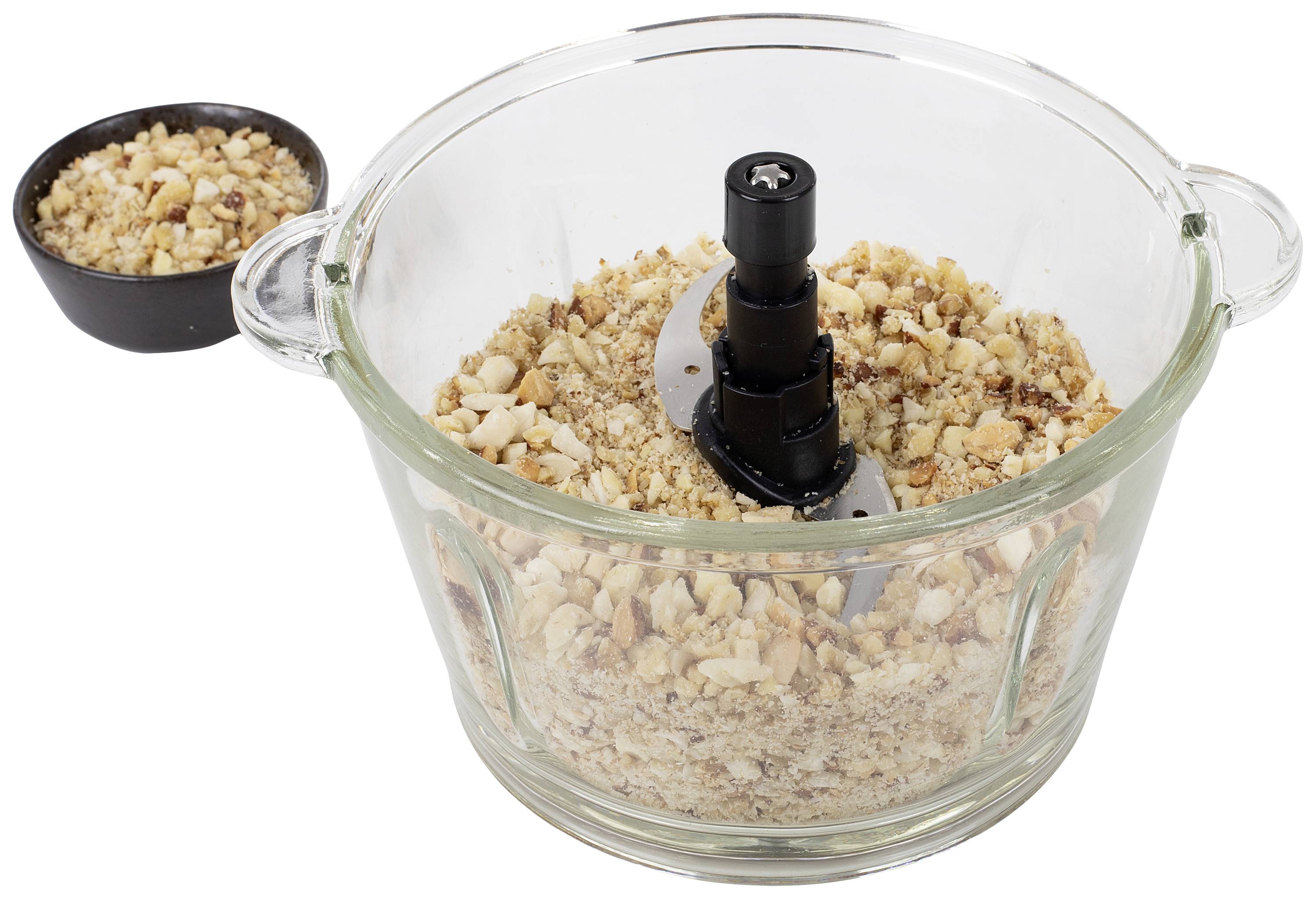 Szklany pojemnik z ostrzem do rozdrabniania zawiera posiekane orzechy, obok stoi mała miseczka z dodatkowymi posiekanymi orzechami.