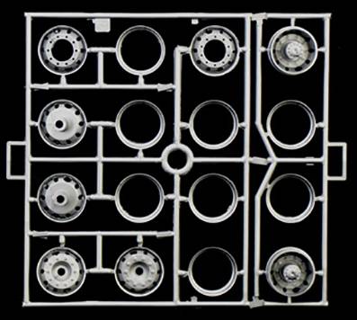 Kilka części o kształcie kołowym w plastikowej ramce, prawdopodobnie elementy zestawu modelarskiego, na czarnym tle.