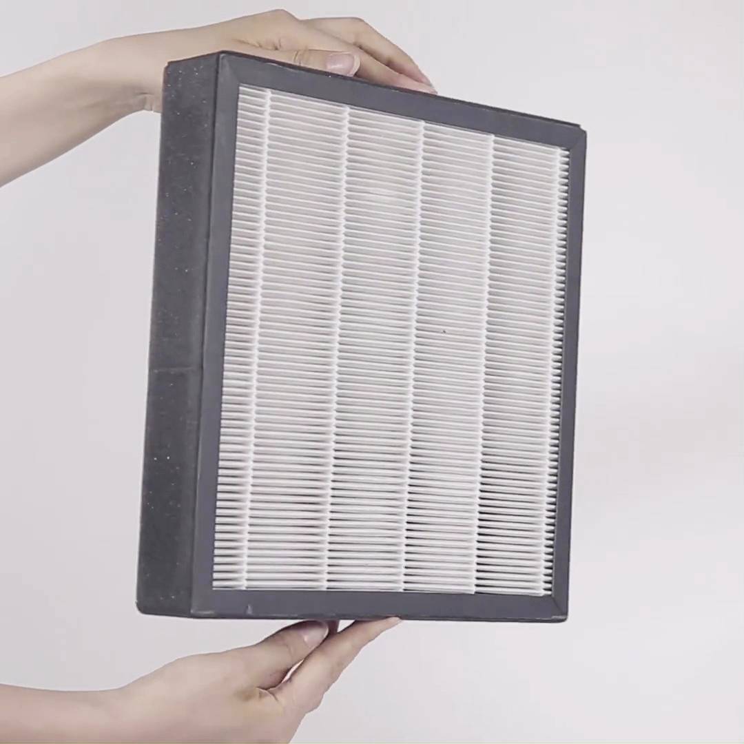 Osoba trzyma prostokątny, biały filtr powietrza z czarną ramką. Filtr jest prezentowany w poziomie na neutralnym tle.