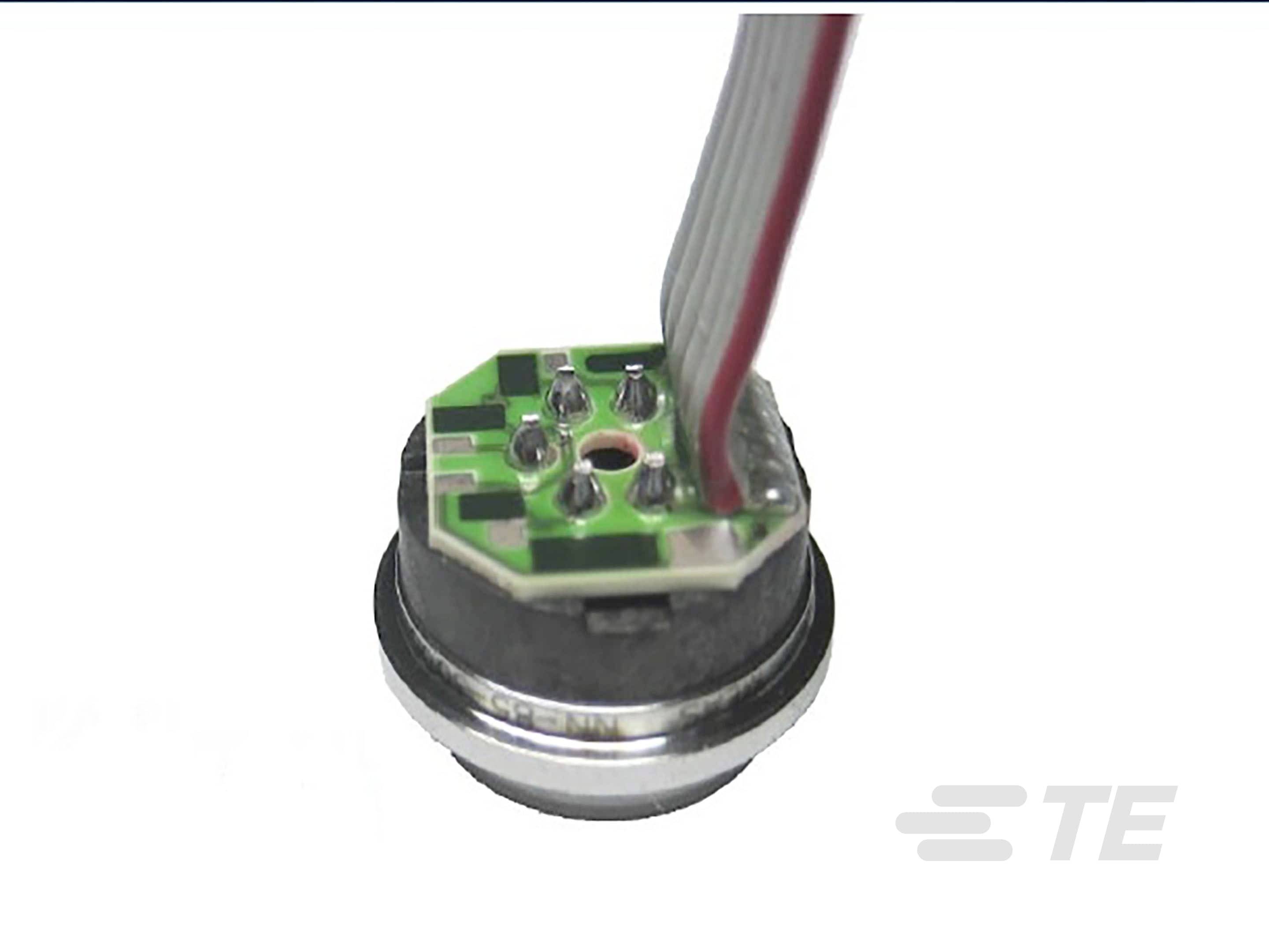 Elektroniczny podzespół z okrągłą podstawą i wieloma stykami metalowymi, do którego podłączony jest płaski, wielożyłowy kabel.