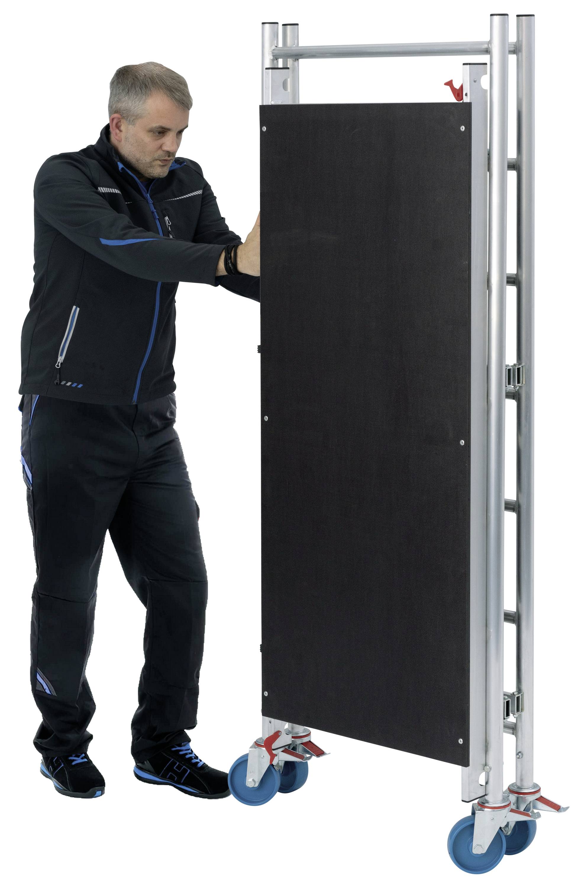 Osoba przesuwa składany wózek transportowy z niebieskimi kółkami, który przewozi dużą prostokątną płytę.