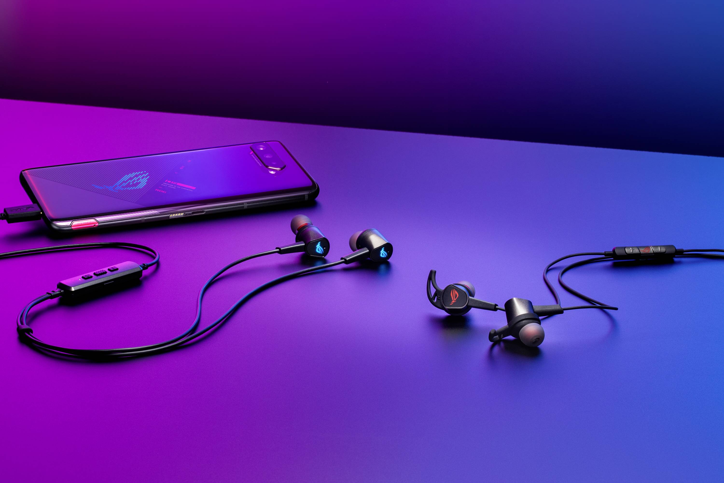 Smartfon leży obok słuchawek dokanałowych na stole. Ekran smartfona jest podświetlony, a słuchawki są podłączone.