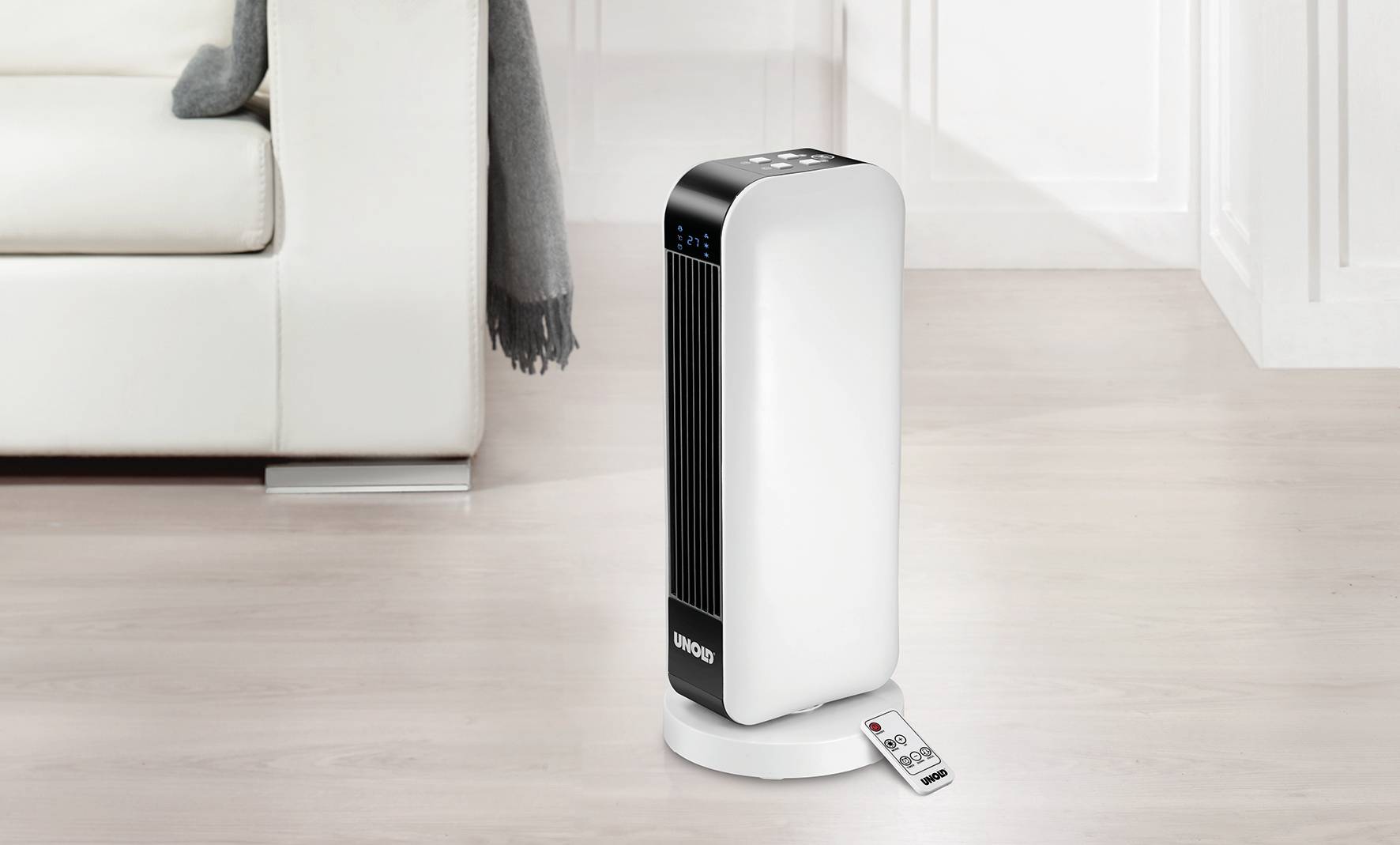 Oczyszczacz powietrza stojący w salonie na podłodze, obok kanapy. Przed nim leży pilot.