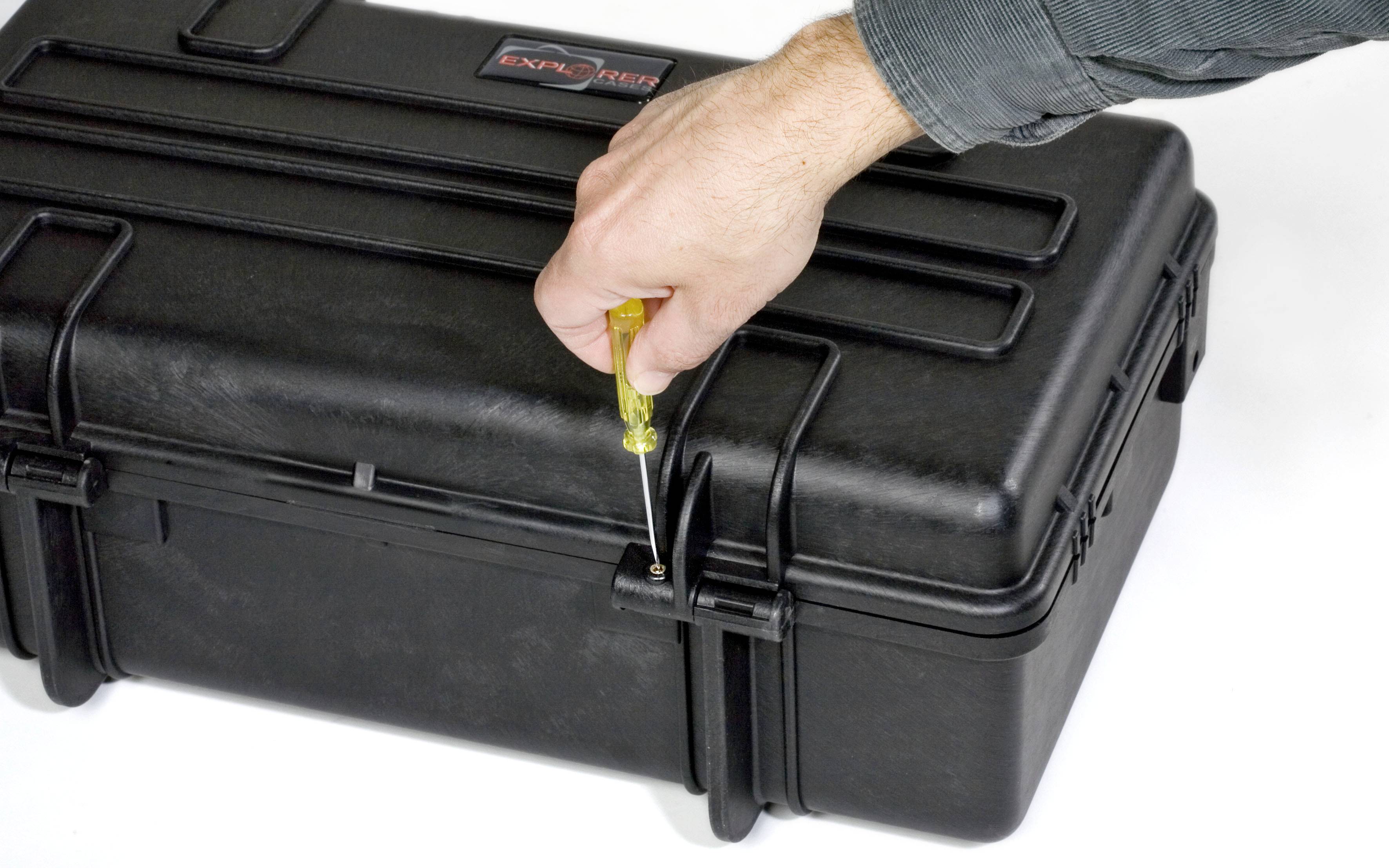 Śrubokręt jest używany do otwarcia czarnej, wytrzymałej obudowy ochronnej. Jedna ręka trzyma śrubokręt.