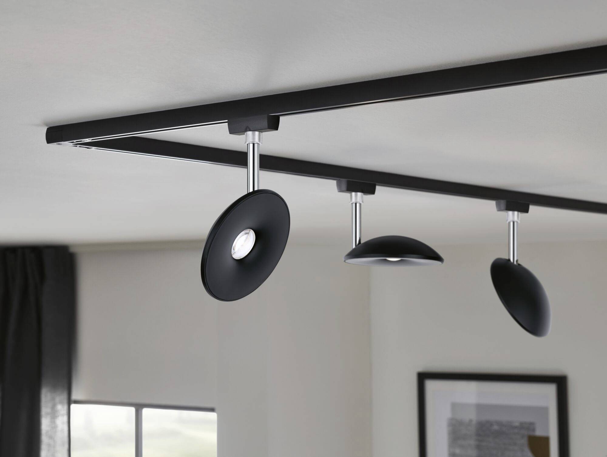 Nowoczesna czarna lampa sufitowa z trzema indywidualnie regulowanymi reflektorami oświetla pomieszczenie o neutralnych dekoracjach ściennych.