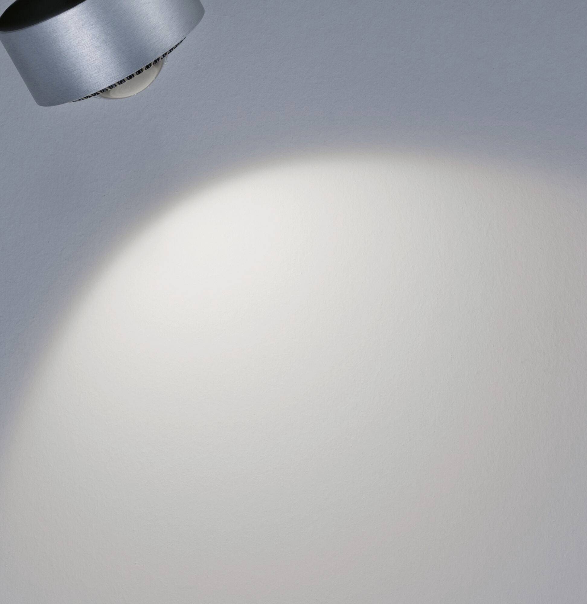 Lampa sufitowa rzuca okrągły stożek światła na szarą ścianę, tworząc jasny obszar w ciemnym otoczeniu.