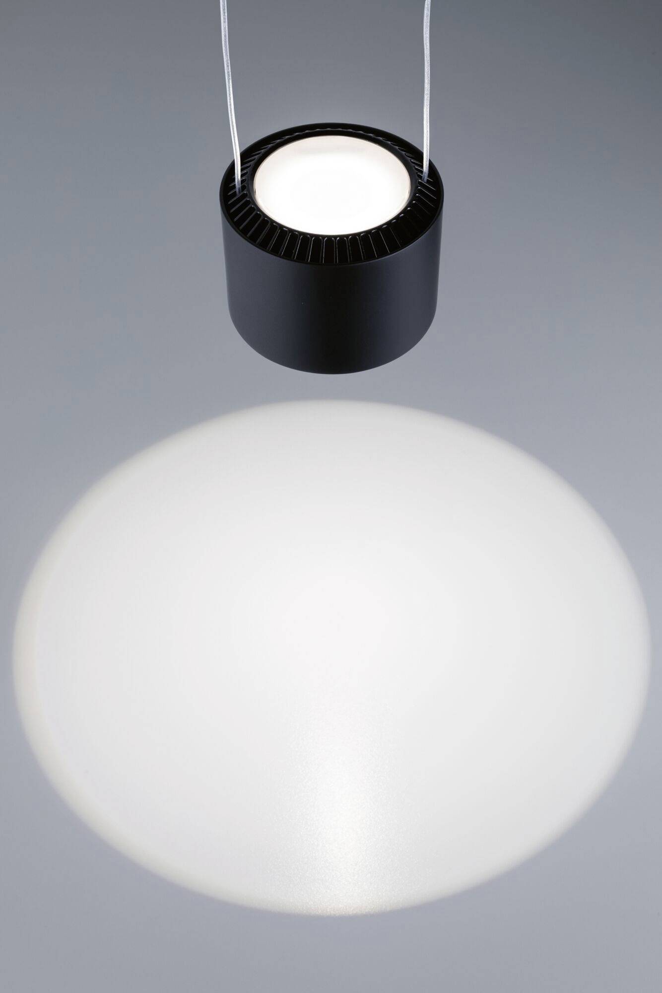 Czarna lampa wisząca oświetla okrągły obszar na powierzchni poniżej.