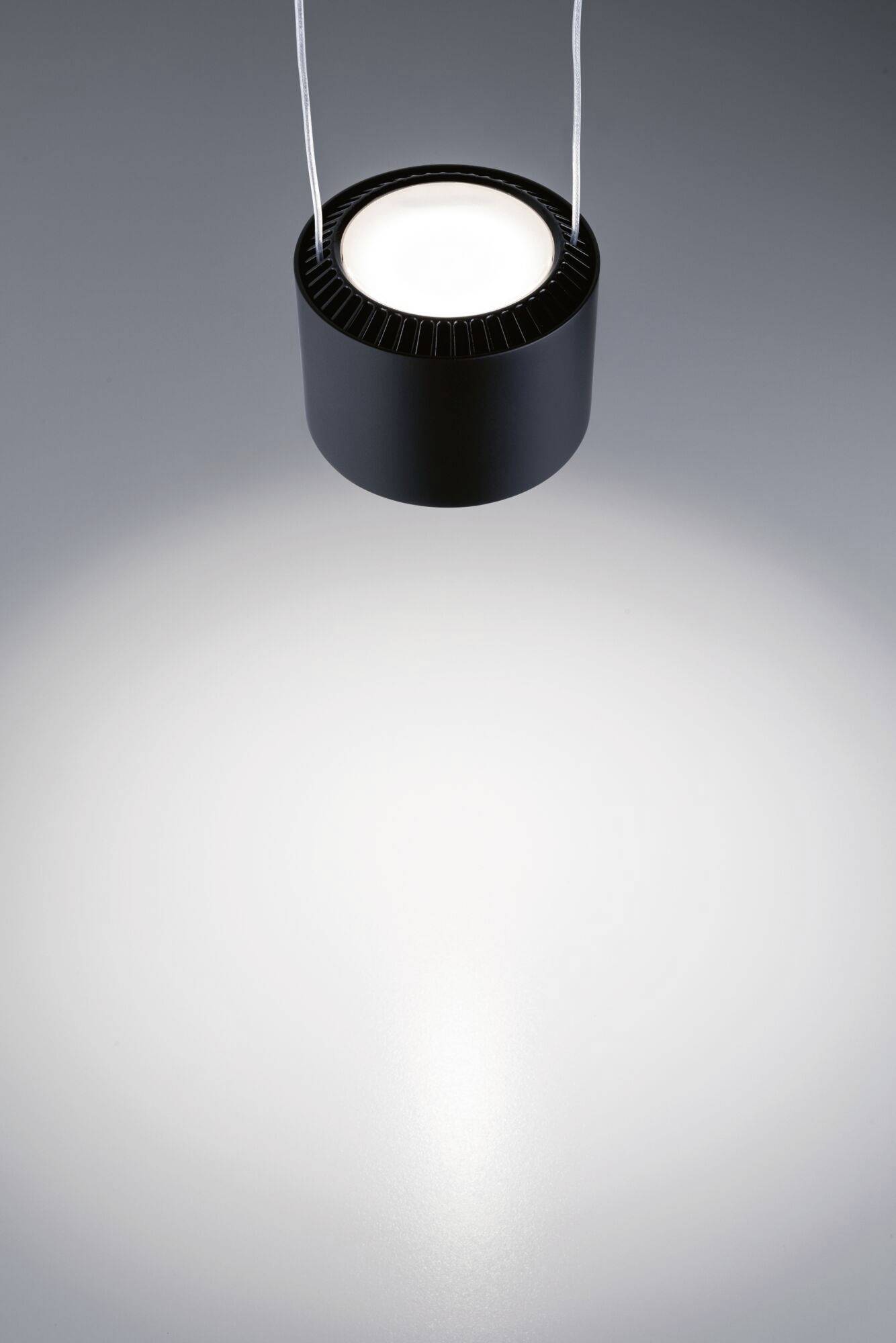 Czarna metalowa lampa wisząca oświetla okrągłą przestrzeń na szarej powierzchni.