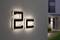 Numer domu '2c' na podświetlonej ścianie. W tle widoczna jest część budynku z wejściem.