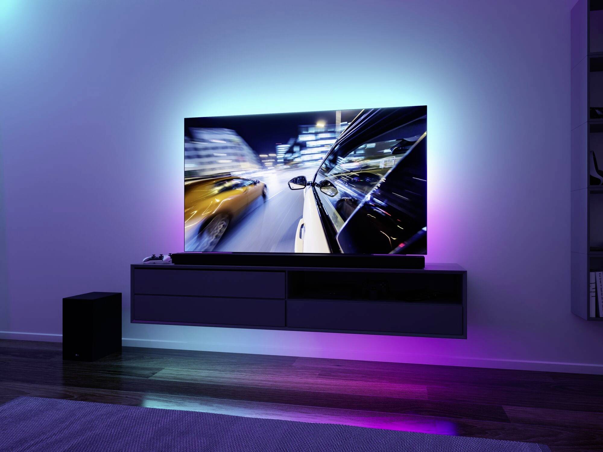 Stylowy pokój z dużym telewizorem plazmowym zamontowanym na ścianie, na którego ekranie wyświetlany jest obraz przejeżdżających samochodów w oświetlonym mieście.