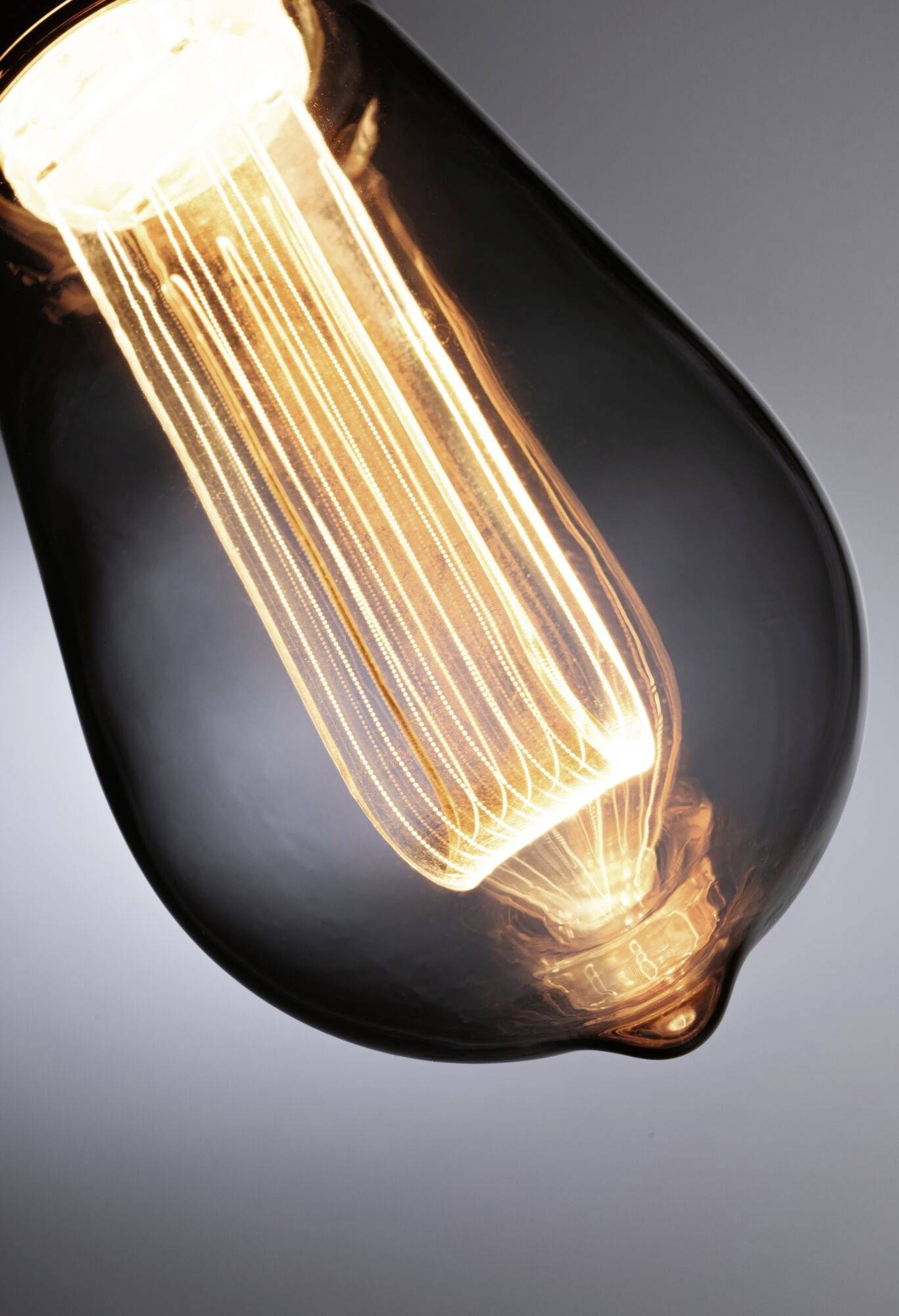 Żarówka z widoczną żarówką, emitująca ciepłe światło, sfotografowana w ciemnym otoczeniu.