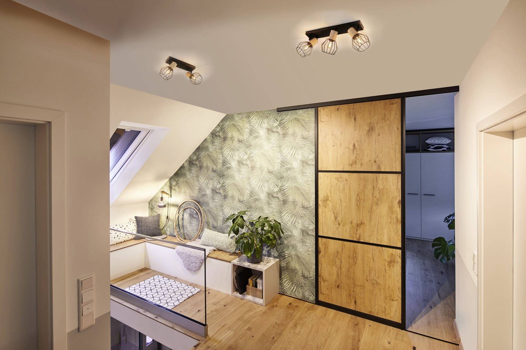 Nowoczesny, dobrze oświetlony poddasze z akcentami drewnianymi i roślinnymi. Kącik wypoczynkowy przy oknie, obok duża szafa.