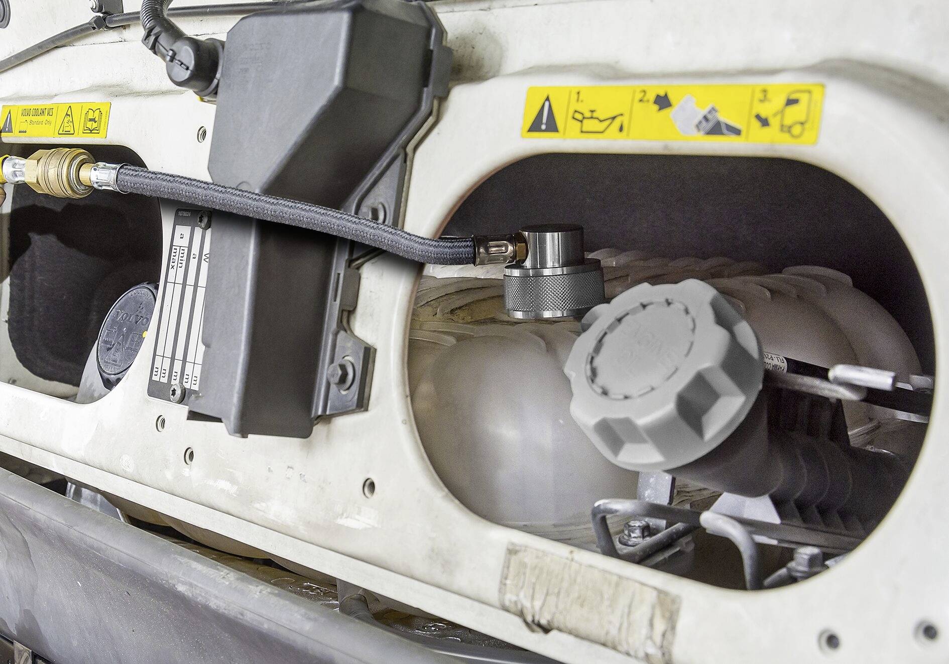 Korek wlewu paliwa ciężarówki otoczony ostrzeżeniami i przewodami połączeniowymi, prezentujący szczegóły konserwacji pojazdu.