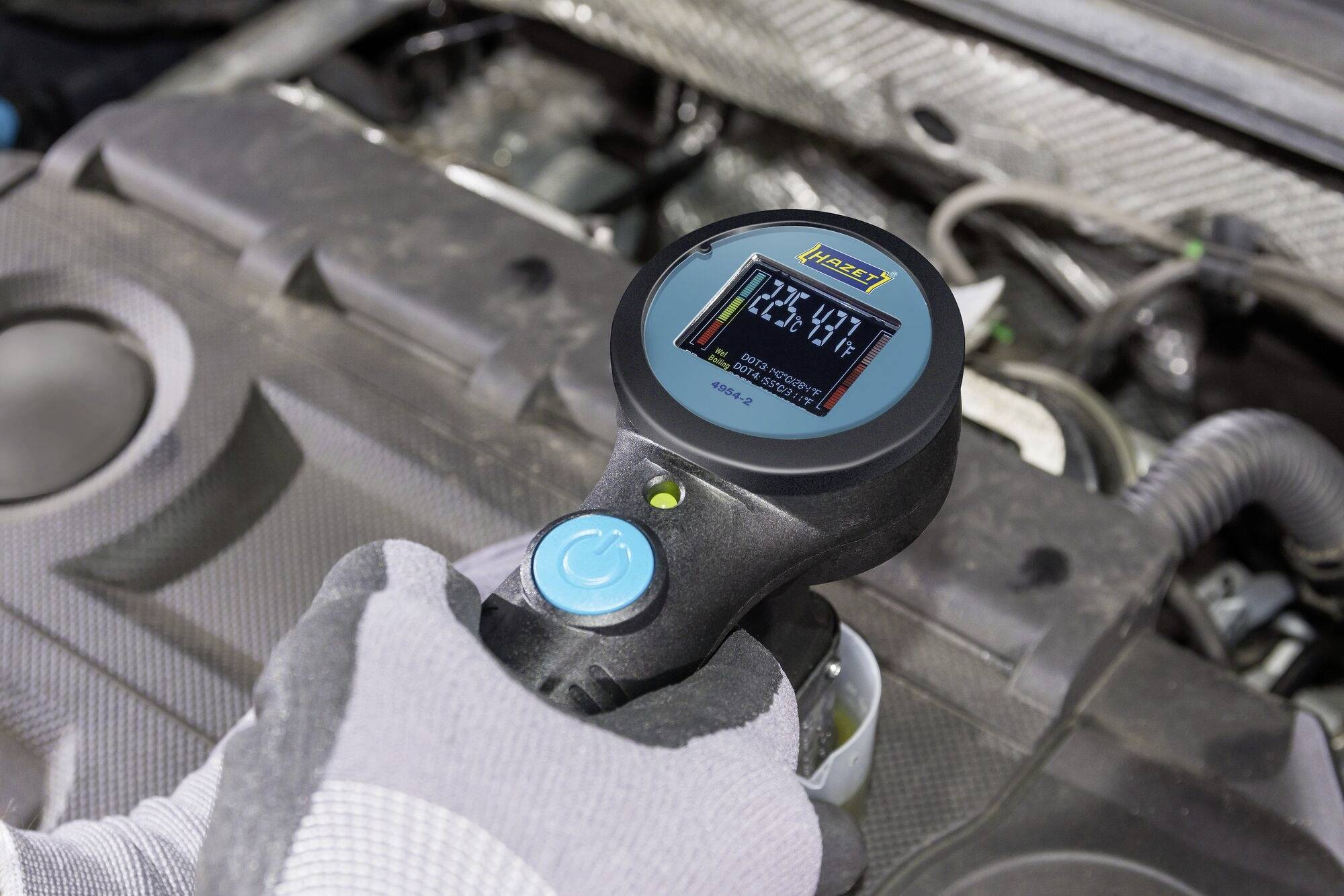 Ilustracja przedstawia osobę w rękawiczkach trzymającą przyrząd do pomiaru ciśnienia w oponach samochodowych nad silnikiem.