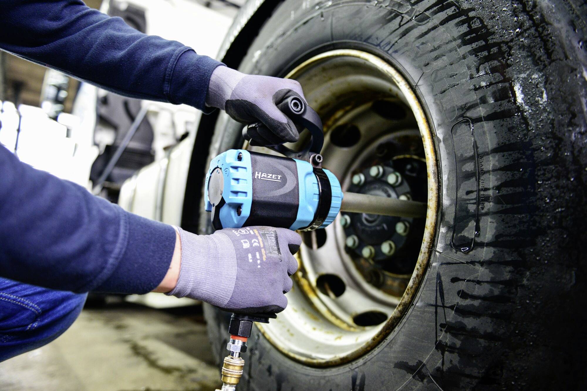 Osoba wymienia oponę pojazdu niebieskim kluczem udarowym w warsztacie.